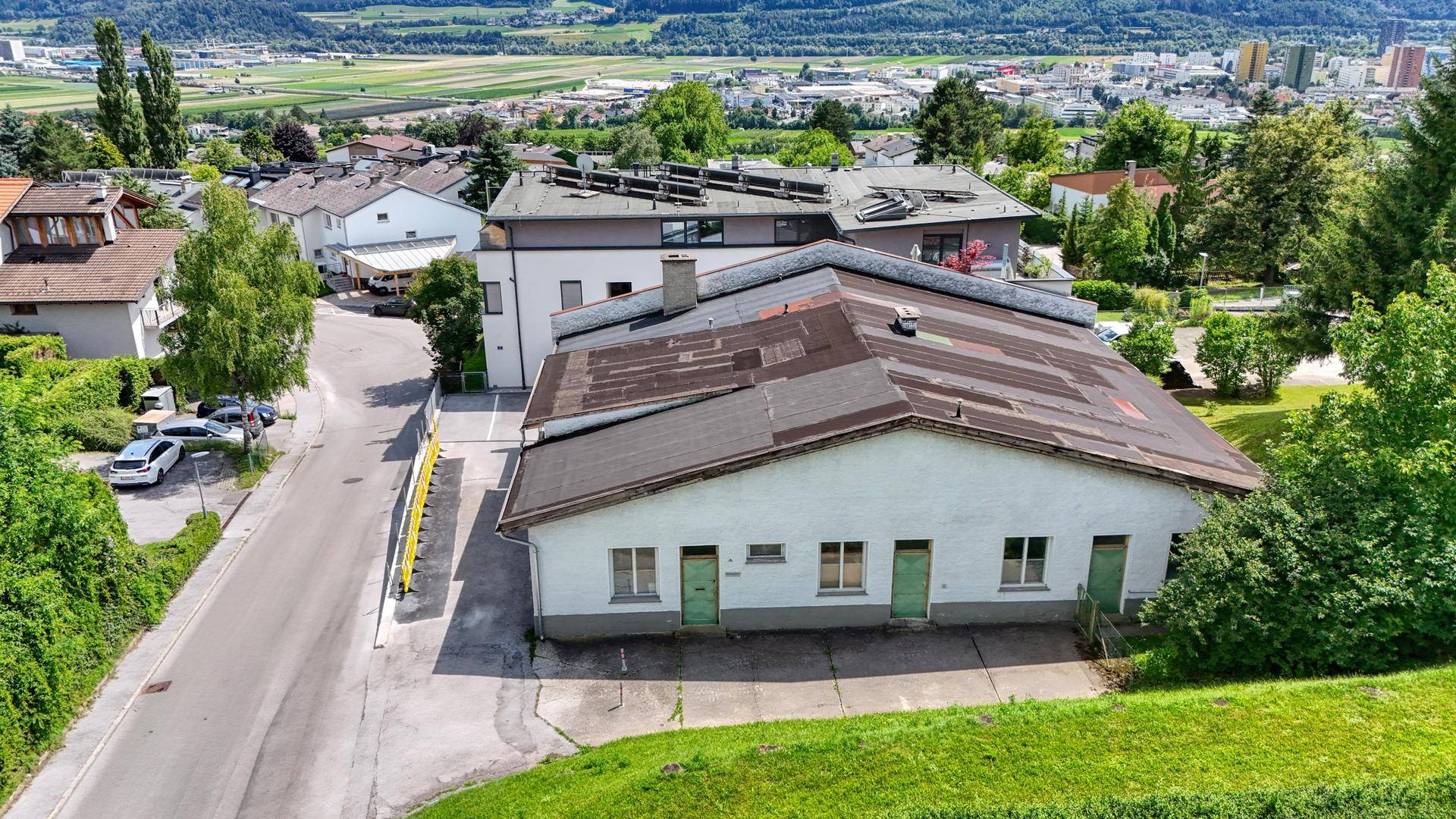 Luftaufnahme eines modernen Gebäudes mit Solaranlagen neben einem längeren, älteren Bauwerk.