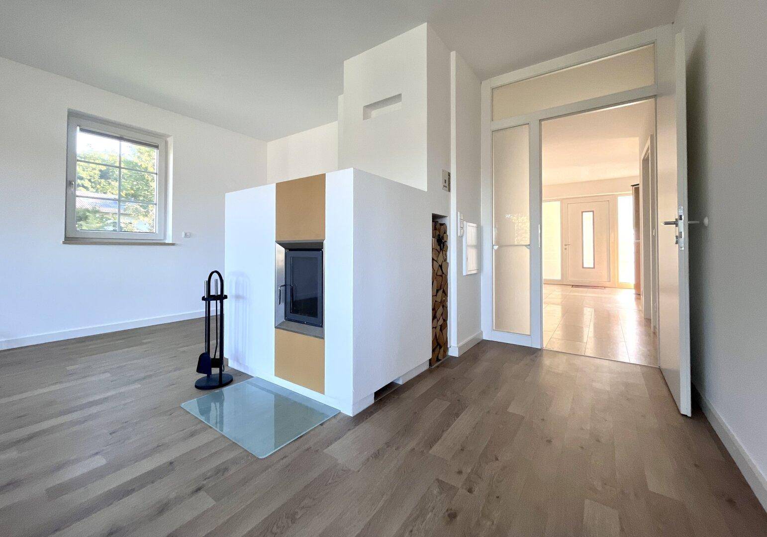 Heller Wohnbereich mit modernem Kamin und Holzablage, durchflutet von natürlichem Licht.