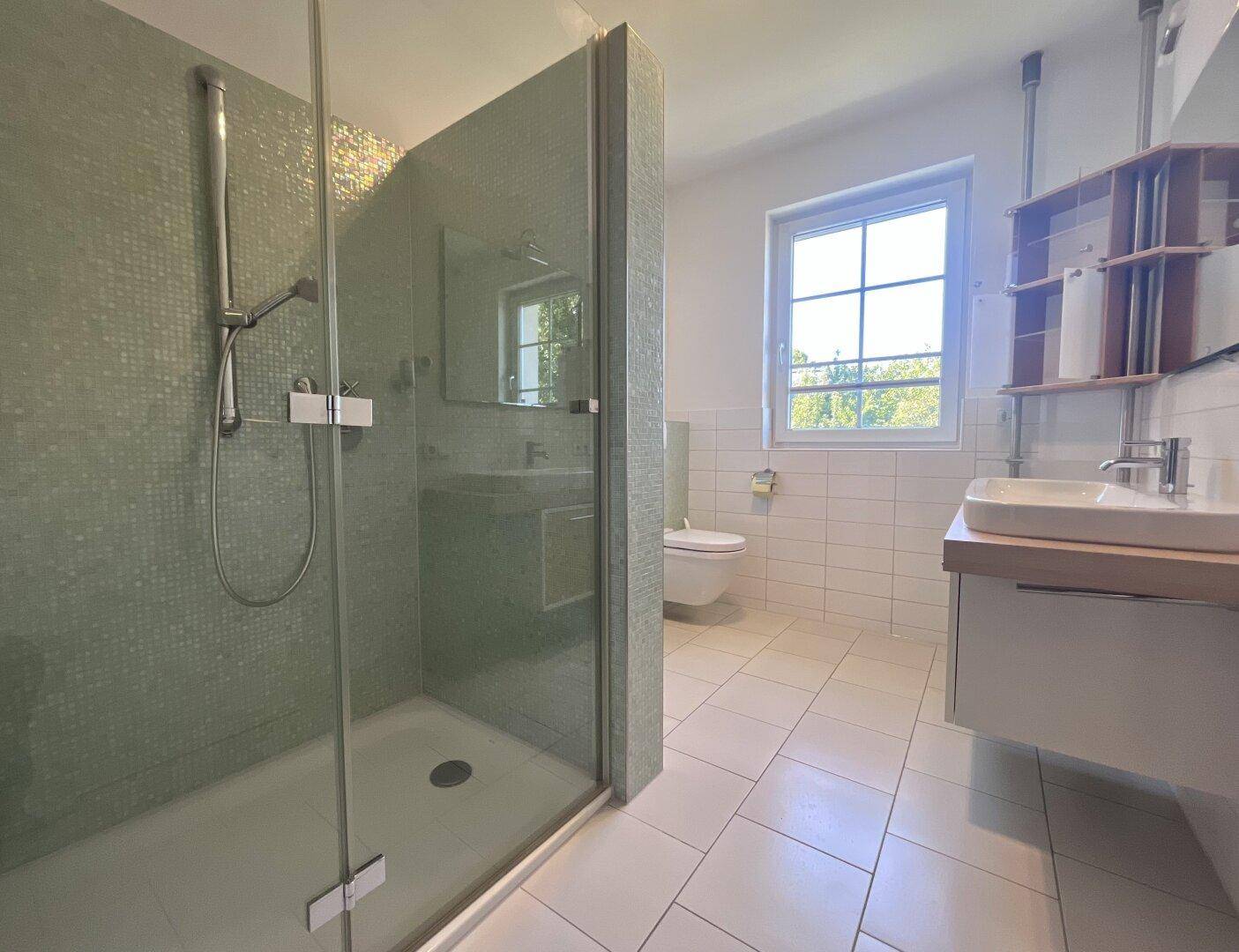 Helles Badezimmer mit großer Duschkabine, WC und Fenster für natürliche Belüftung.