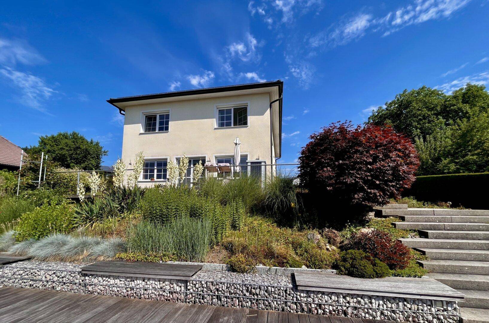 Rückseite des Hauses mit gepflegtem Garten, Steintreppen und einer Terrasse.