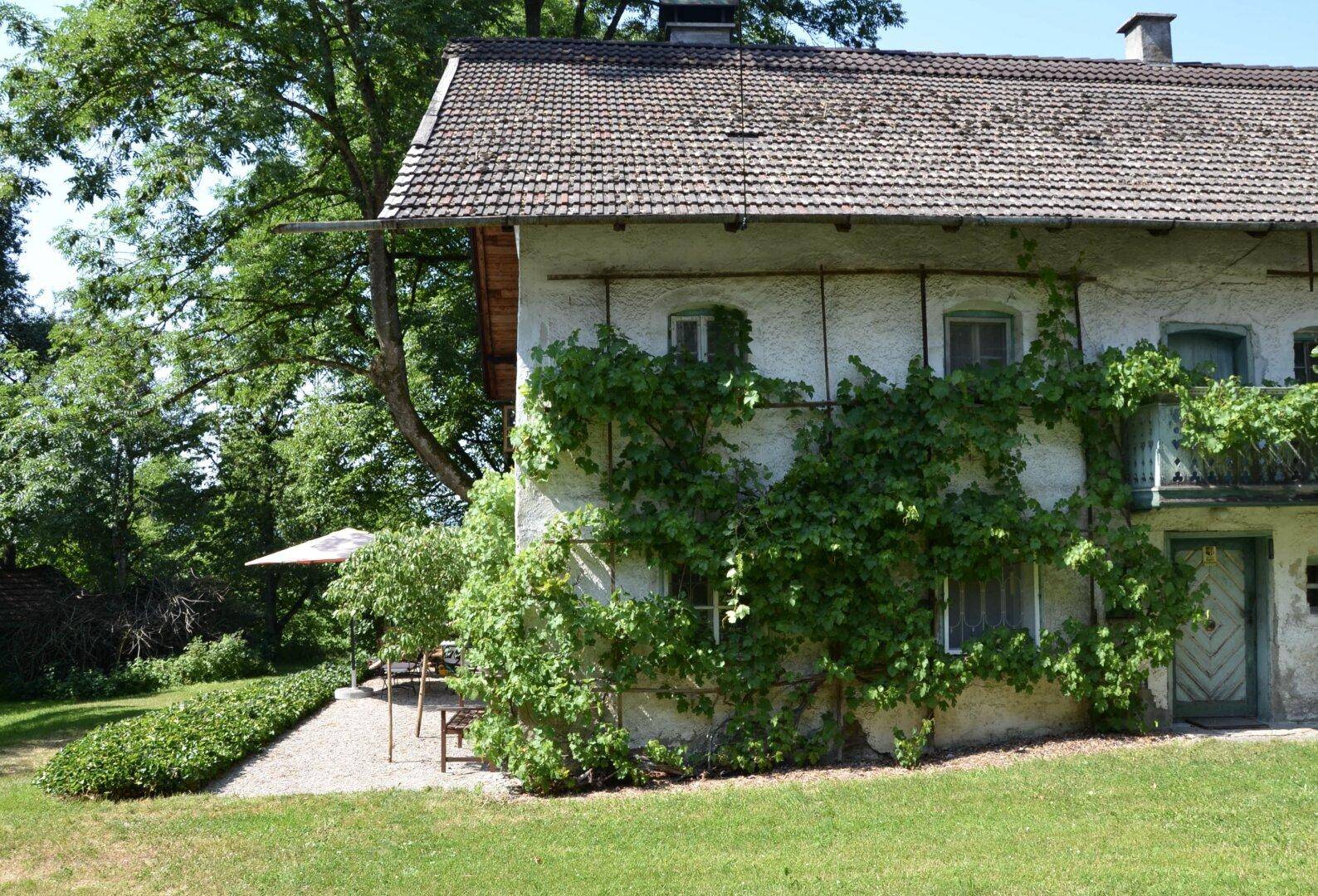 Traditionelles Haus mit bewachsener Fassade und einem kleinen, schattigen Sitzbereich im Garten.