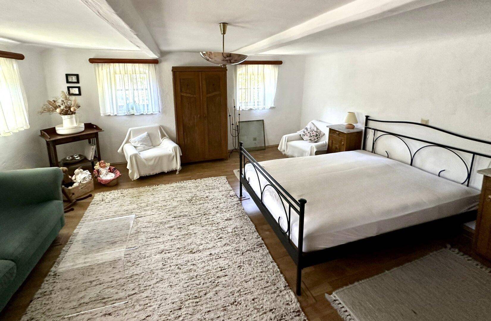 Geräumiges Schlafzimmer mit Doppelbett, großem Teppich und zwei Fenstern für natürliches Licht.
