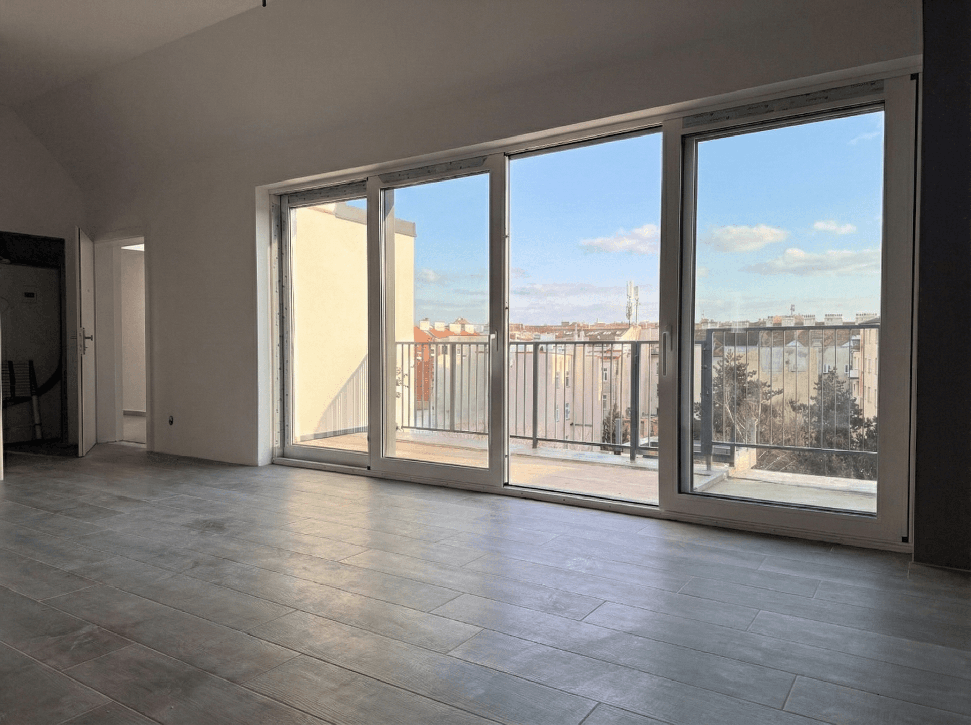 Heller, leerer Wohnbereich mit großen Schiebetüren, Zugang zum Balkon und urbanem Ausblick.
