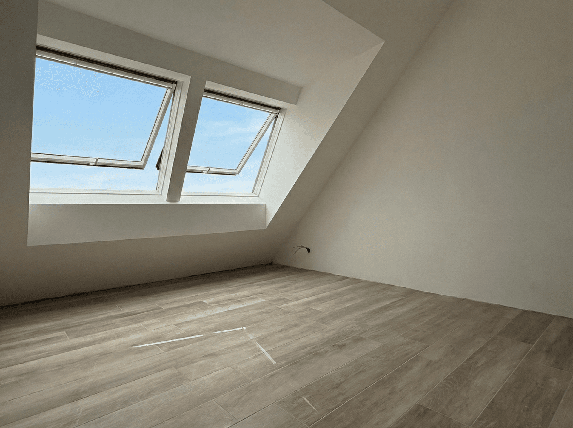 Geräumiges Dachzimmer mit zwei Dachfenstern, hellem Laminatboden und schrägen Wänden.