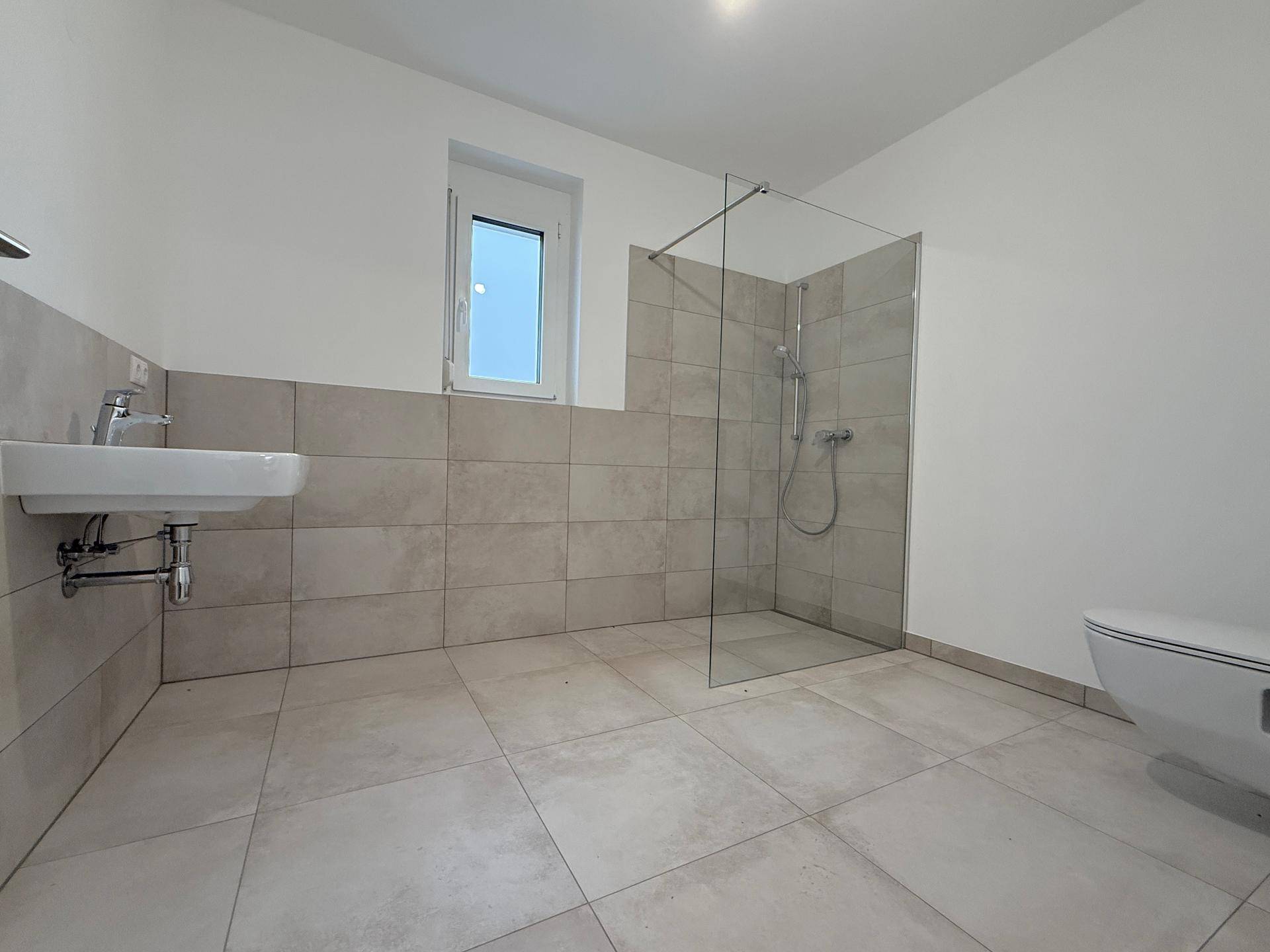 Modernes Badezimmer mit begehbarer Dusche, Wand-WC und hellen Fliesen.