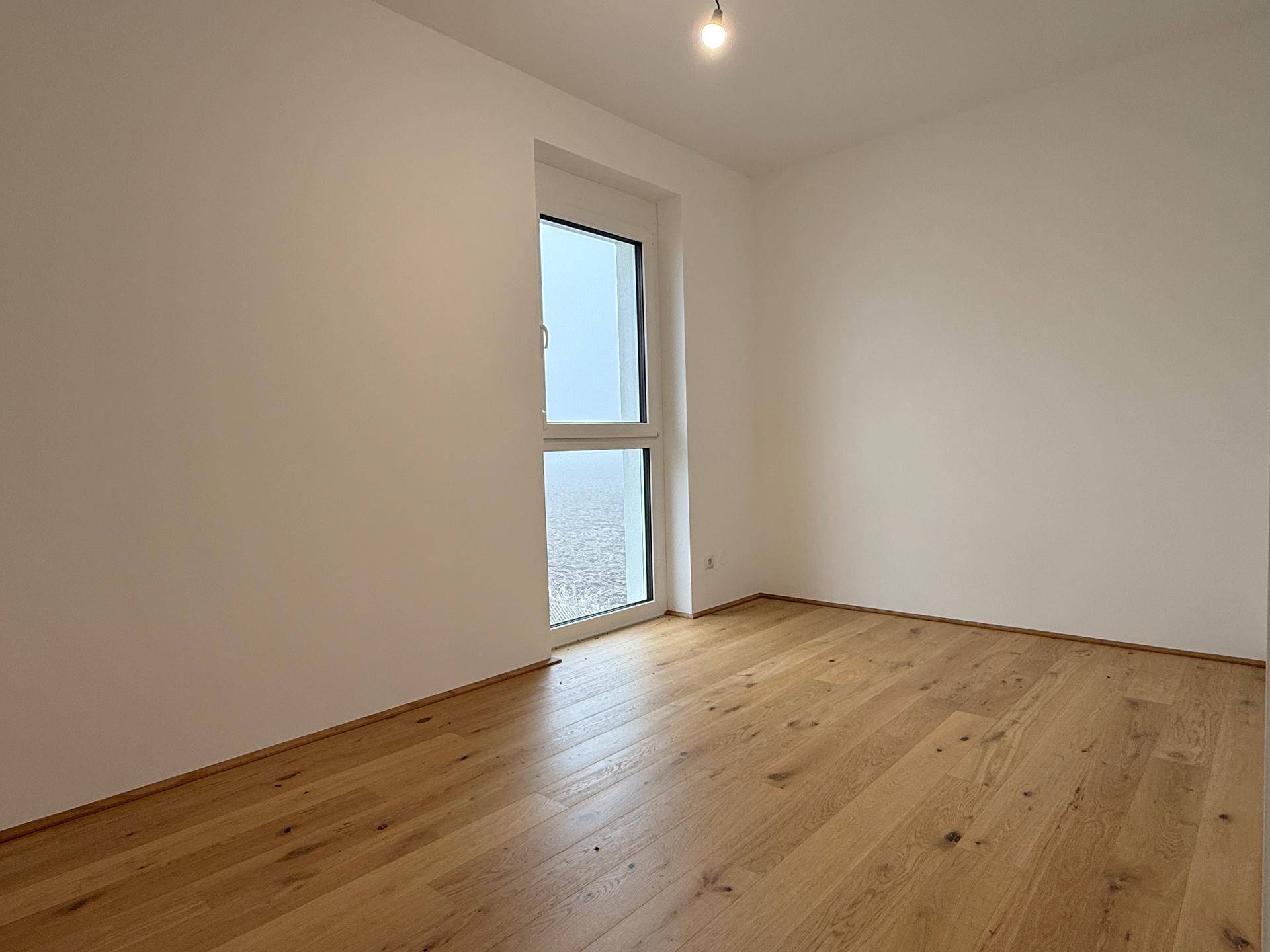 Helles Schlafzimmer mit Holzboden und großer Fenstertür, die viel Tageslicht hereinlässt.