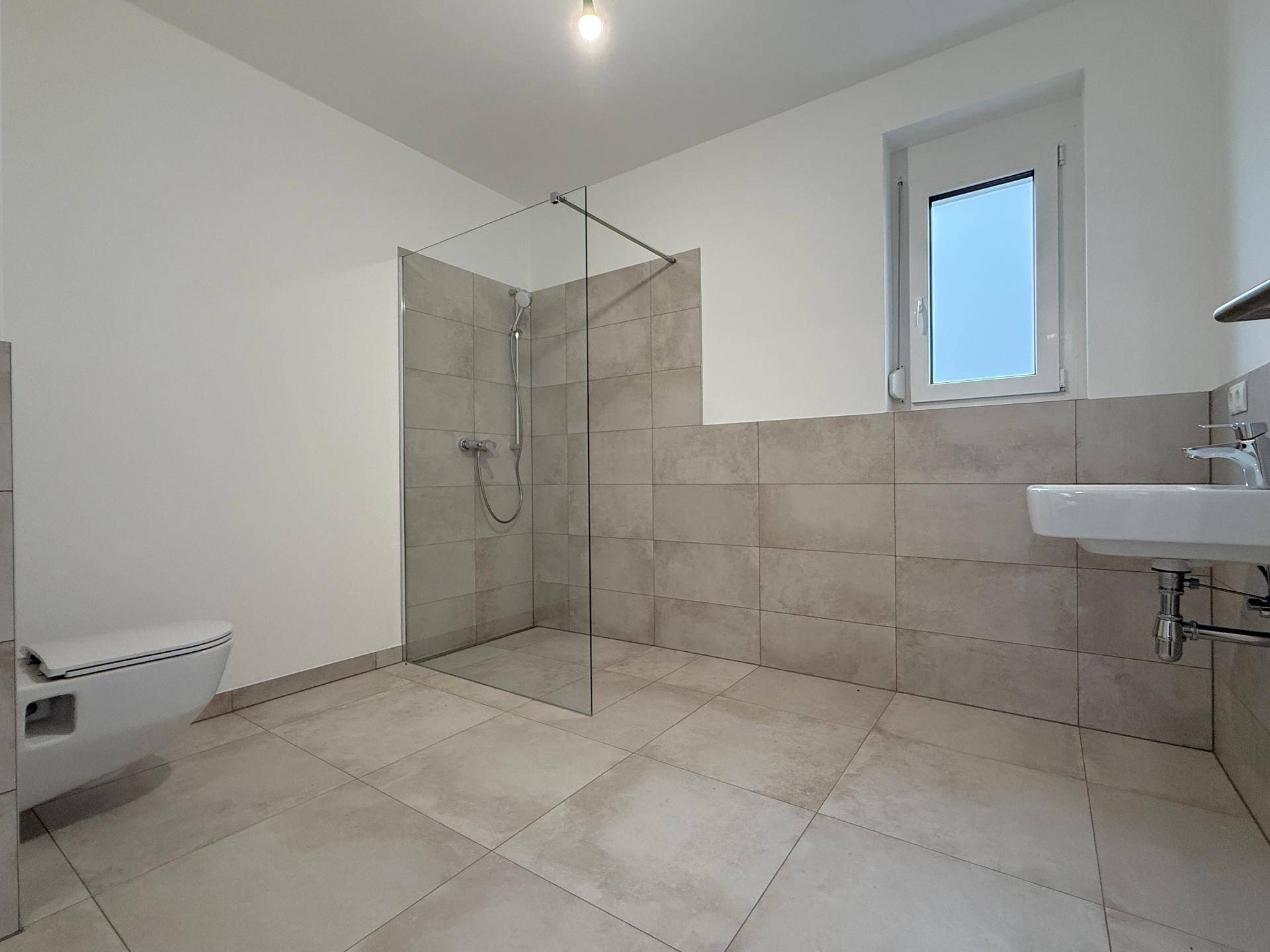 Modernes Badezimmer mit ebenerdiger Dusche, Wand-WC und großformatigen Fliesen.