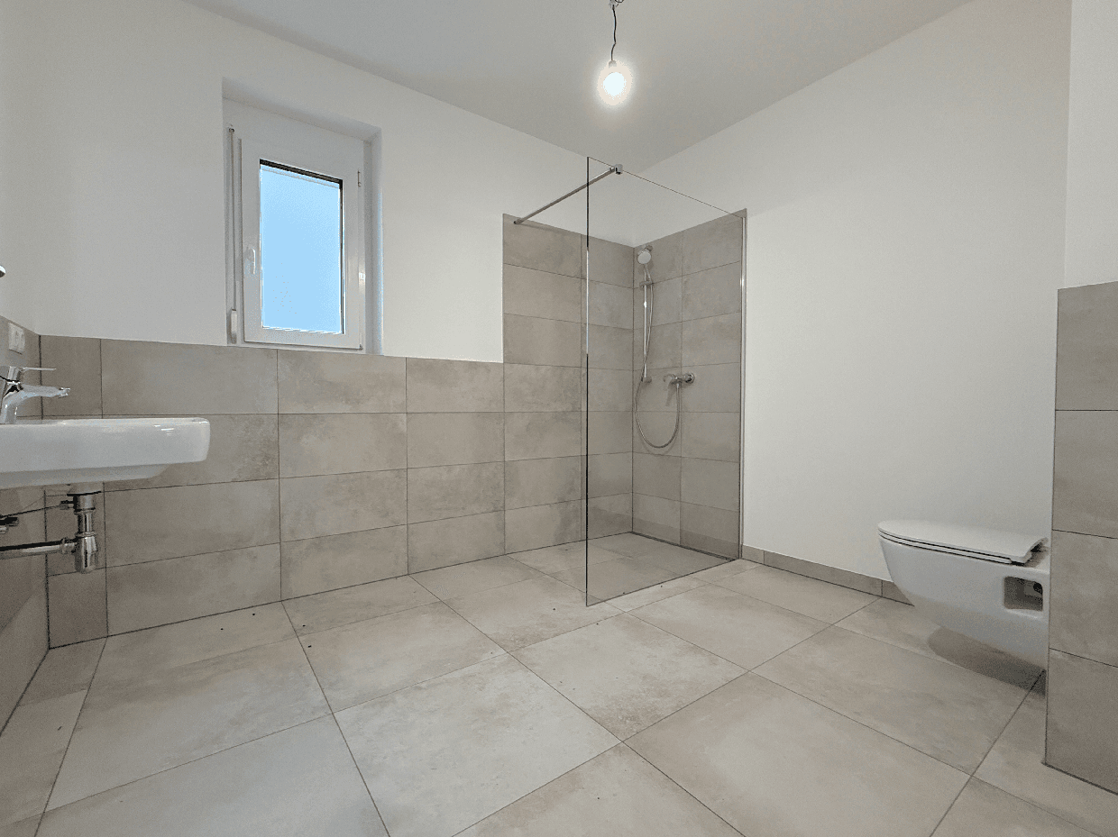Modernes Badezimmer mit hellgrauen Fliesen, ebenerdiger Dusche und Fenster.