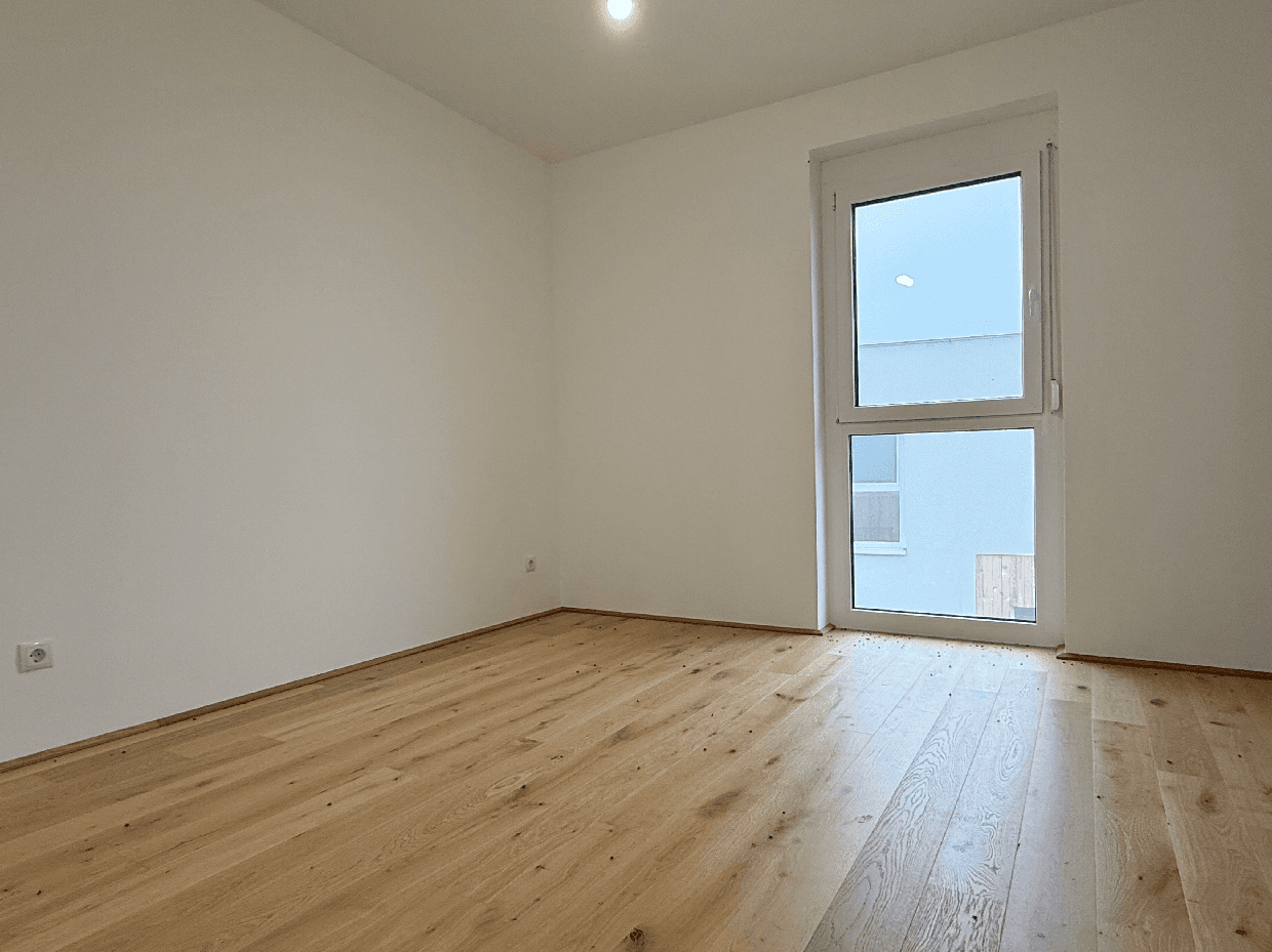 Helles Schlafzimmer mit Eichenparkettboden und großem Fenster, bereit zur Einrichtung.