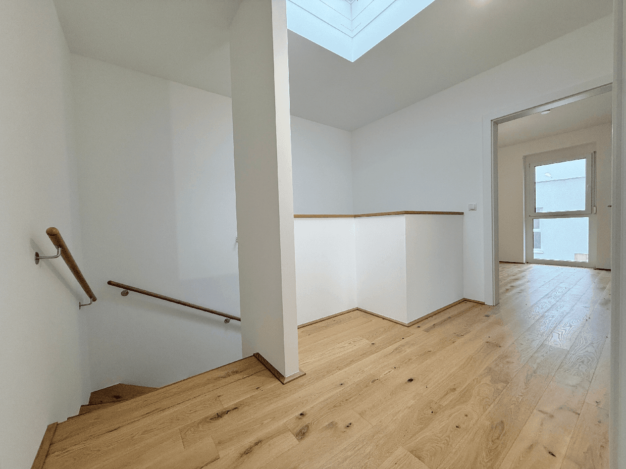 Heller Flur mit Holzparkett, Treppengeländer und natürlichem Licht durch ein Oberlicht.