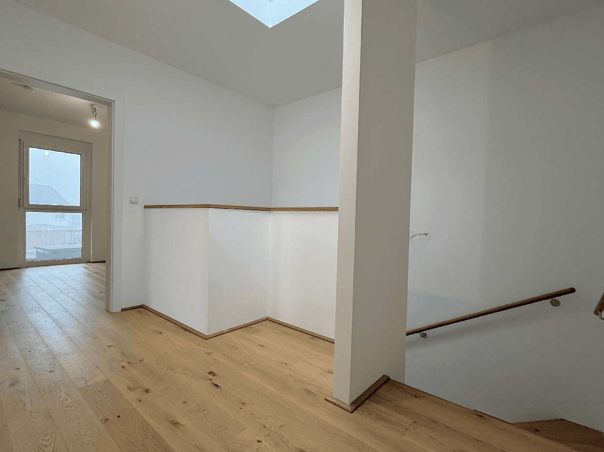 Heller Flur mit Holztreppe, Holzboden und Oberlicht für natürliches Licht.