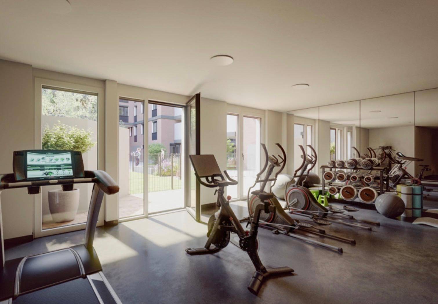 Moderner Fitnessraum mit verschiedenen Trainingsgeräten und großen Fenstern zum Außenbereich.