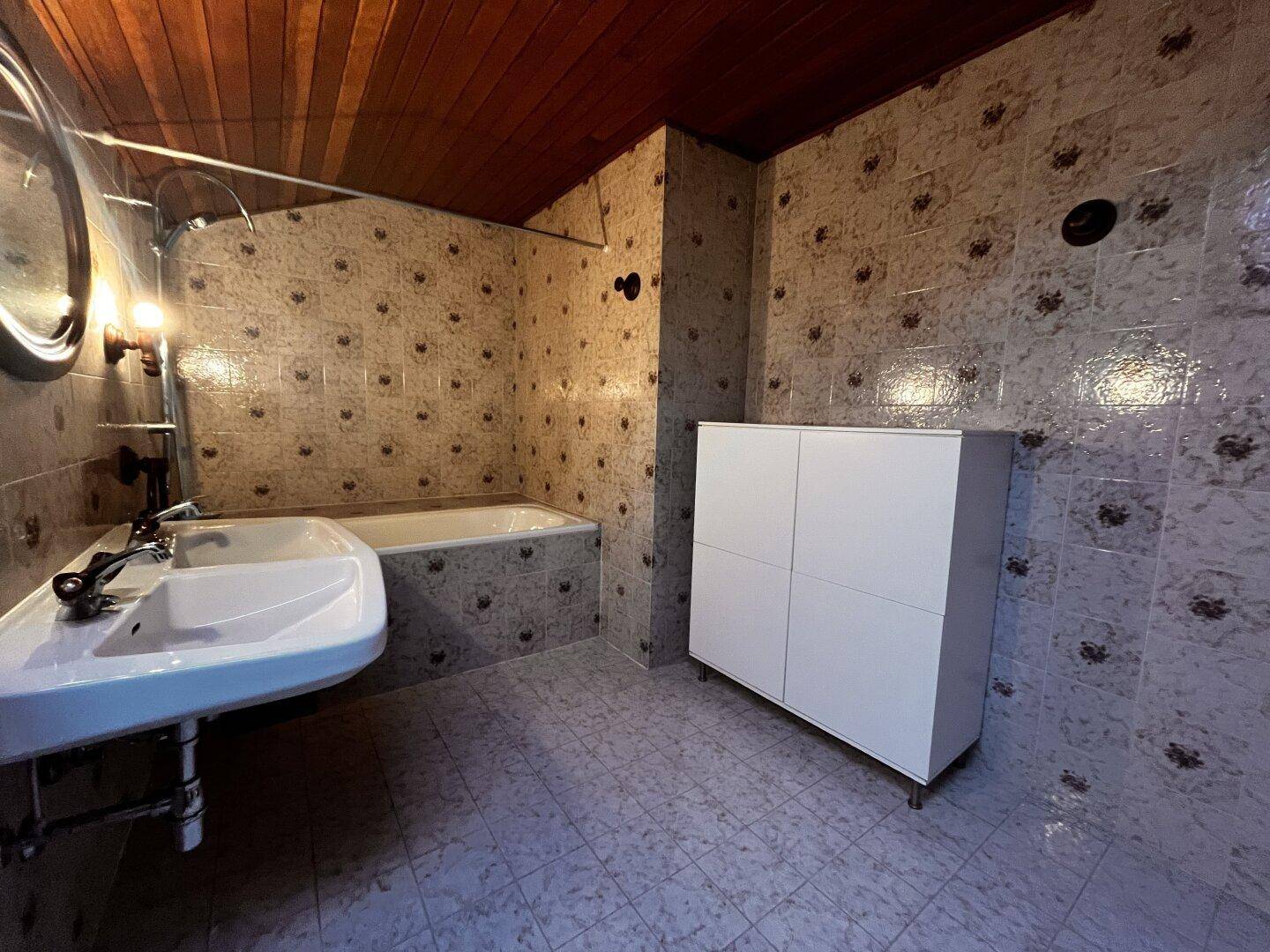 Badezimmer mit gemusterten Fliesen, Badewanne, Waschbecken und Holzdecke.