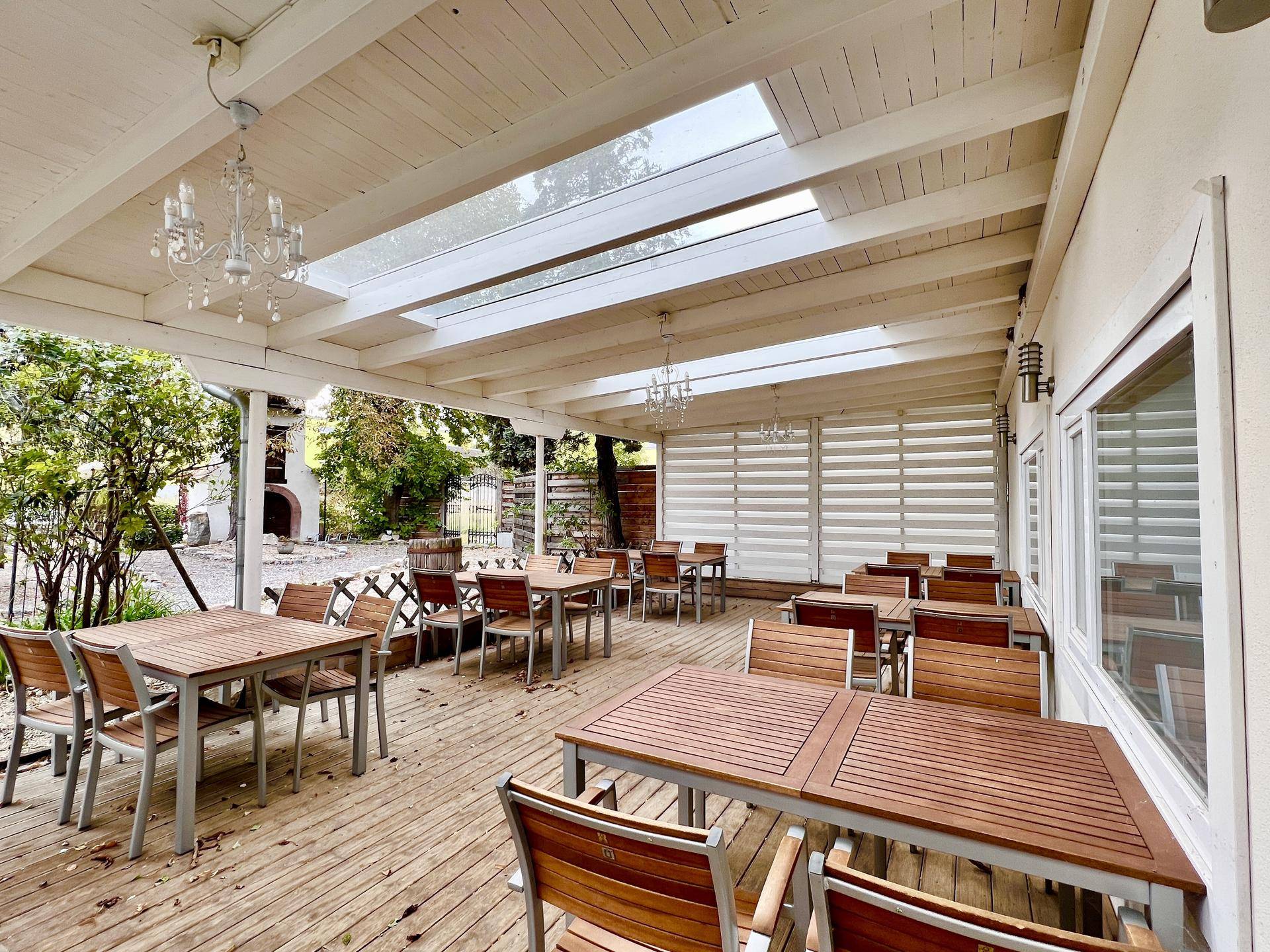 Überdachte Terrasse mit Holzboden, Tischen und Stühlen für Gäste, ausgestattet mit Oberlichtern.