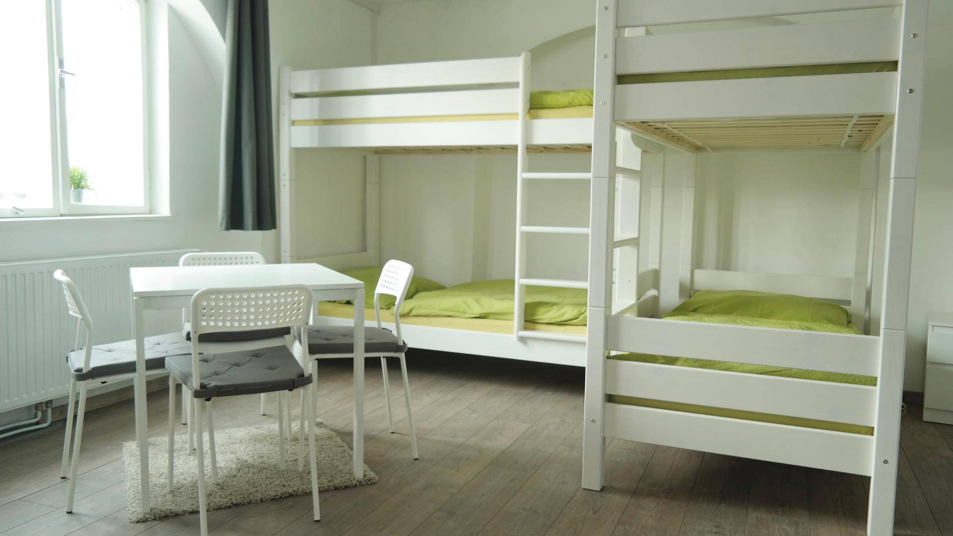 Helles Schlafzimmer mit zwei Etagenbetten, Esstisch und Fenster, ideal für Gruppenunterkünfte.