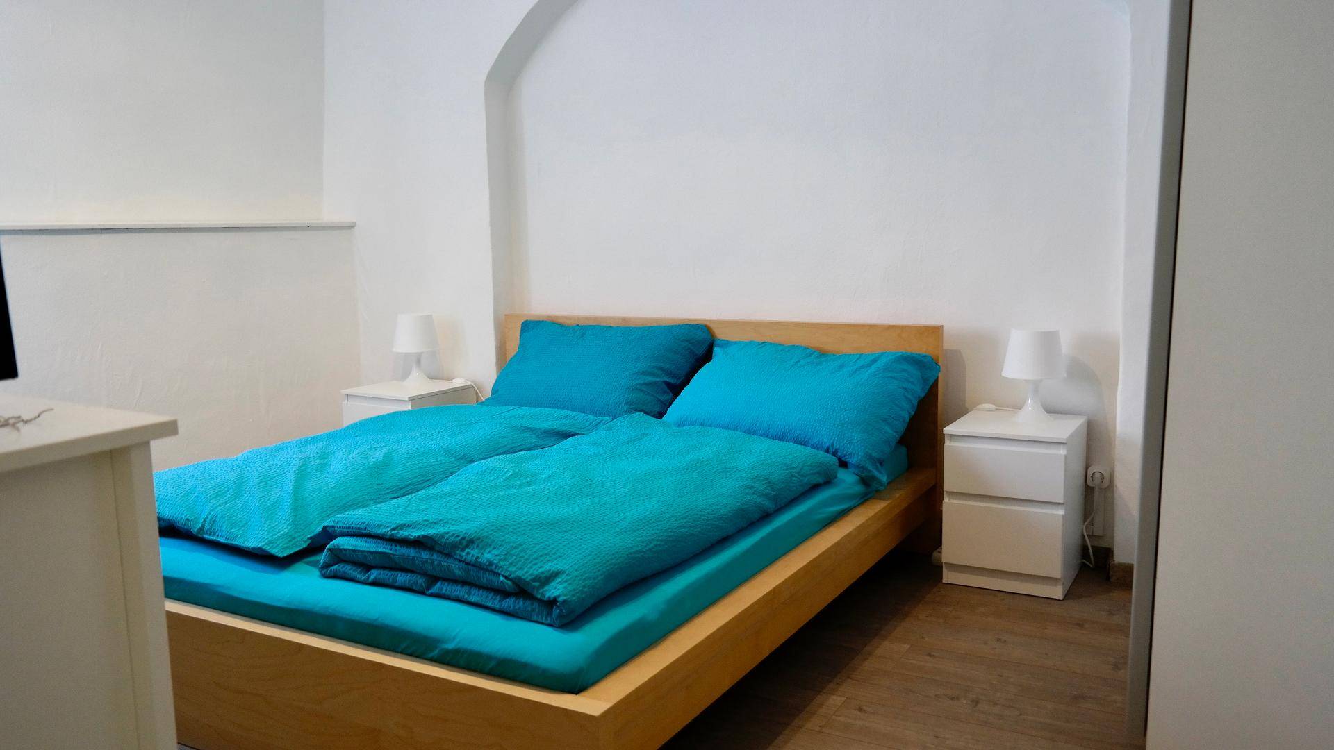 Schlafzimmer mit Doppelbett, Nachttischen und türkisfarbener Bettwäsche in minimalistischem Design.