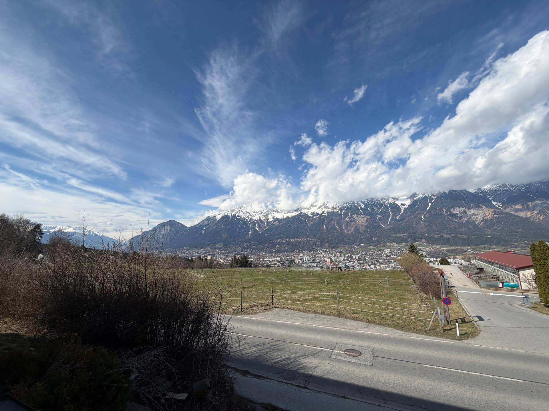 Weitläufiger Blick auf die Berglandschaft und das Tal mit einer Siedlung unter bewölktem Himmel.