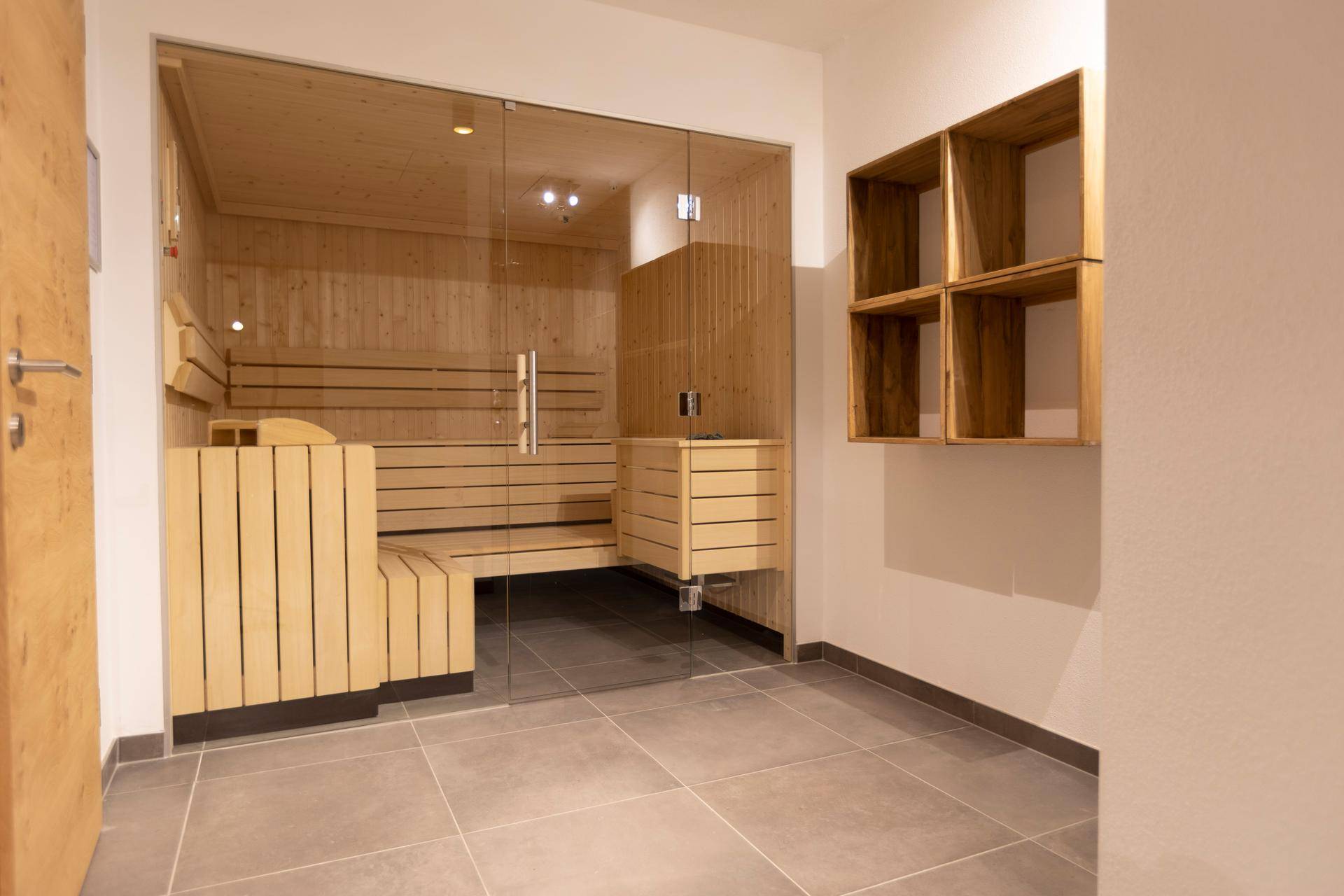 Moderne Sauna mit Holzbänken und Glasfront, Teil eines Wellnessbereichs.