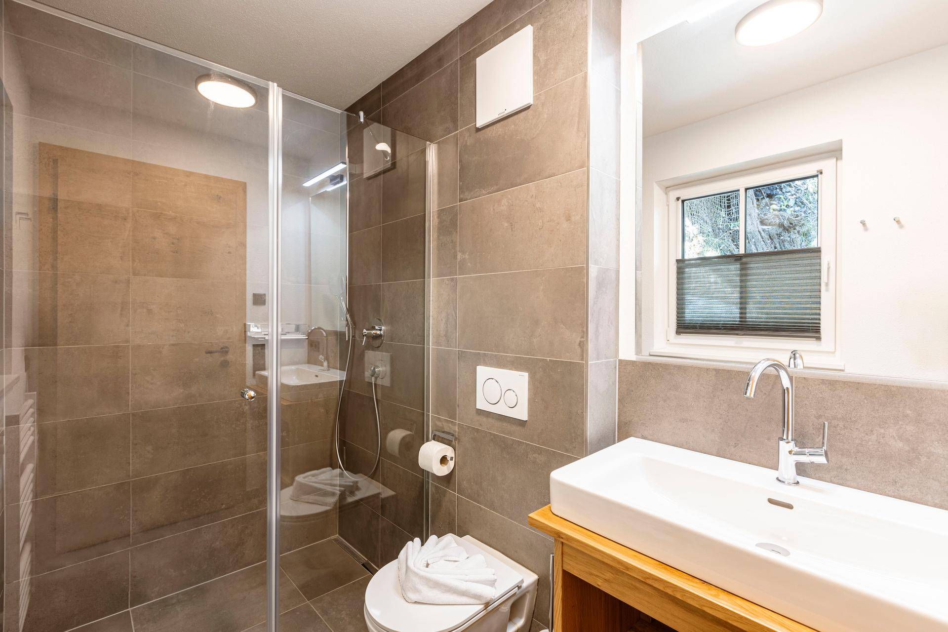 Modernes Badezimmer mit großer Duschkabine, Waschtisch und Fenster für Tageslicht.