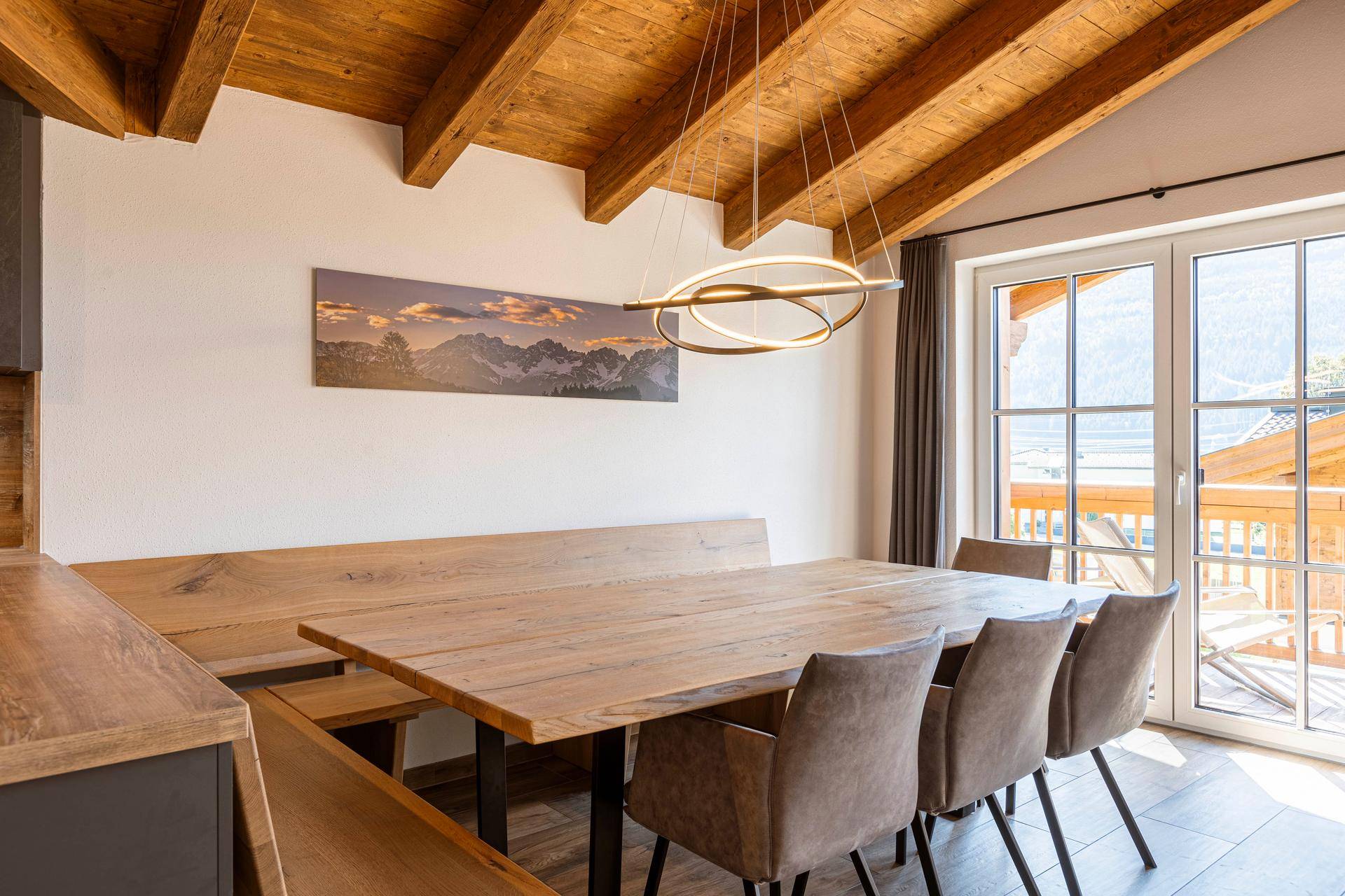 Heller Essbereich mit großem Holztisch, bequemen Stühlen und Zugang zu einem Balkon.
