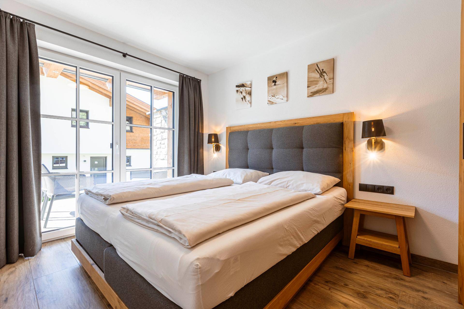 Helles Schlafzimmer mit Doppelbett, Holzboden und Zugang zu einem Außenbereich.