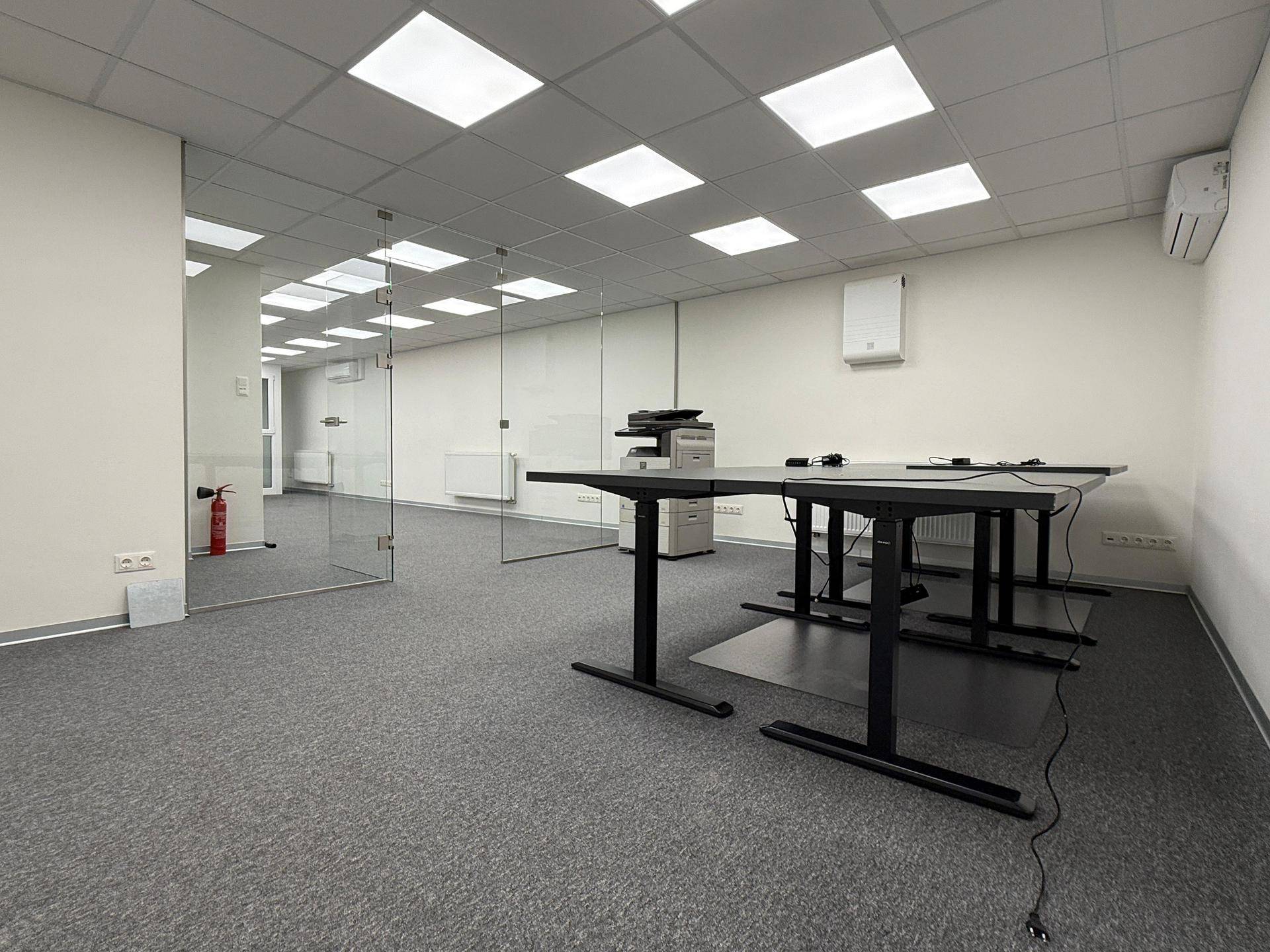 Modernes Büro mit Glastrennwänden, höhenverstellbaren Schreibtischen und Teppichboden, ideal für Arbeitsbereiche.