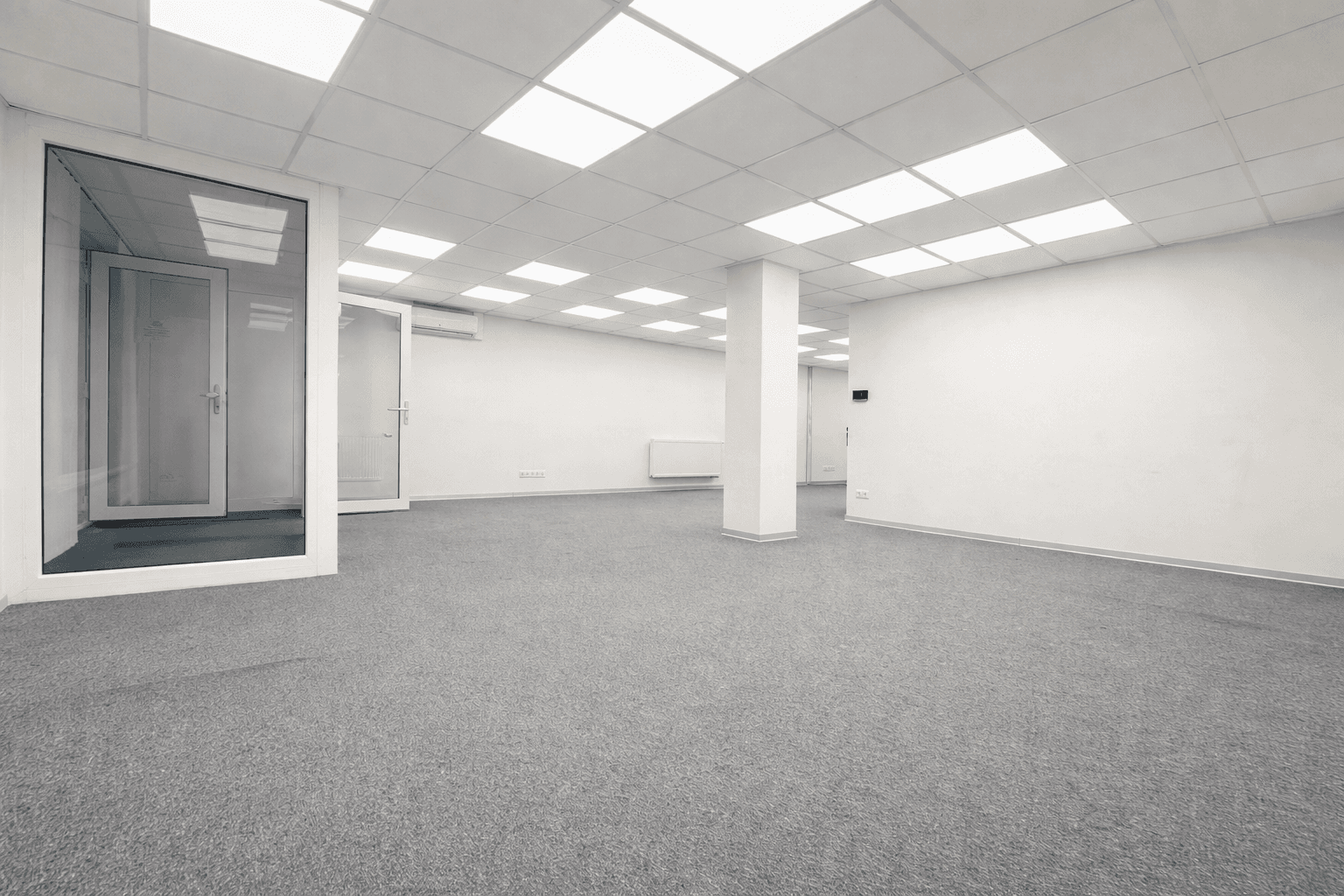 Helles, leeres Büro mit Teppichboden, Säulen und abgehängter Decke, ideal für flexible Bürolösungen.