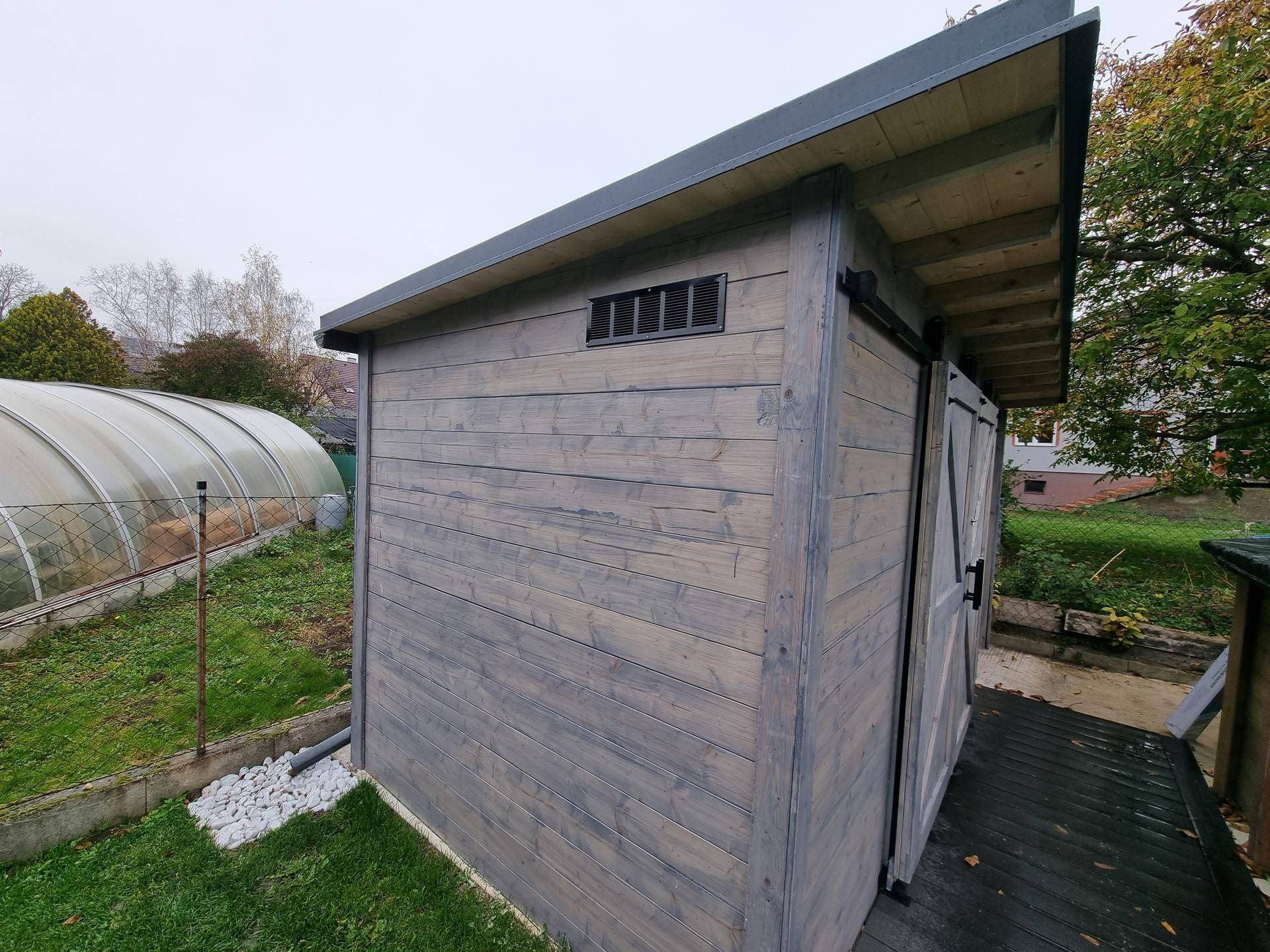 Rustikaler Holzschuppen im Garten mit Pultdach und Schiebetür.