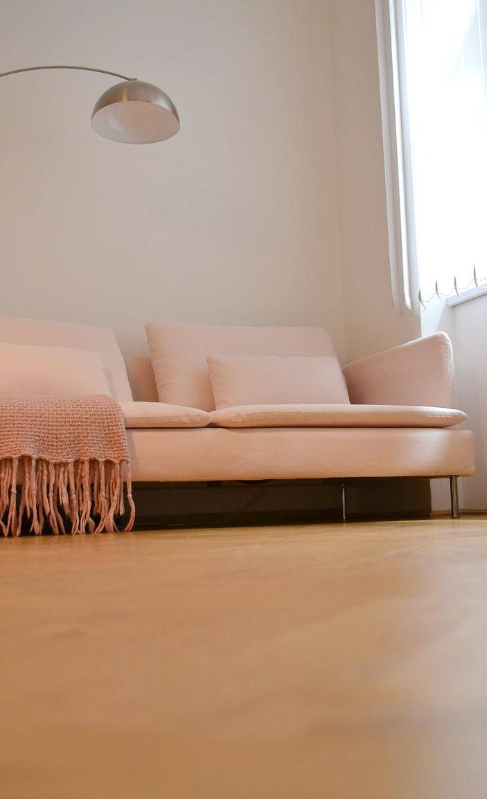 Gemütliches Wohnzimmer mit hellem Sofa, Stehlampe und Holzfußboden.