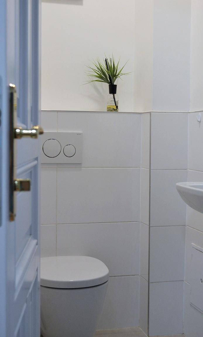 Modernes WC mit wandhängender Toilette und weißen Fliesen.