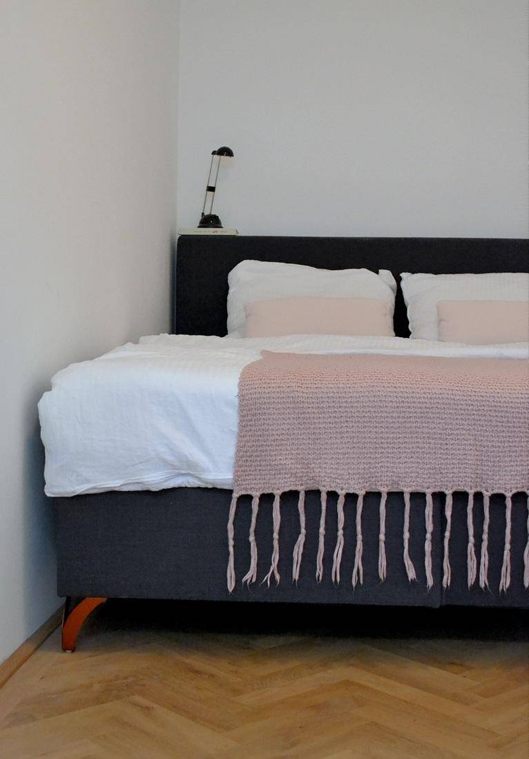 Gemütliches Schlafzimmer mit dunklem Bett, heller Bettwäsche und Fischgrätparkett.