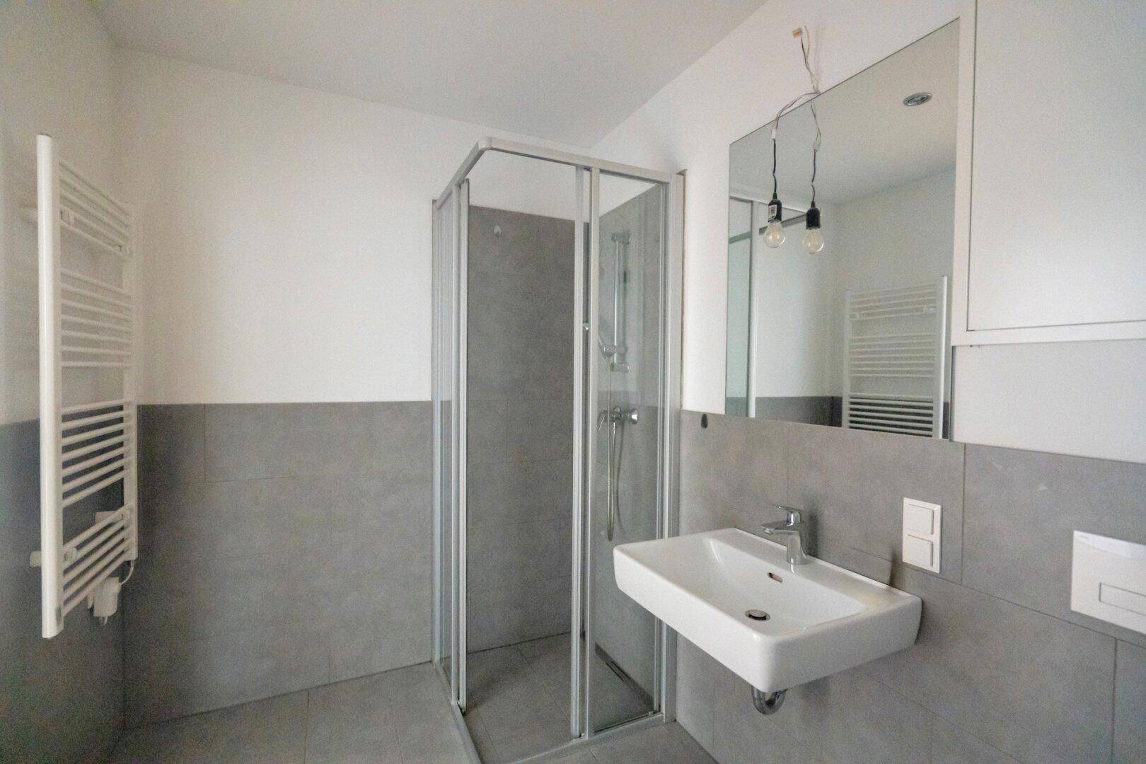 Modernes Badezimmer mit grauen Fliesen, Duschkabine, Waschbecken und beheiztem Handtuchhalter.