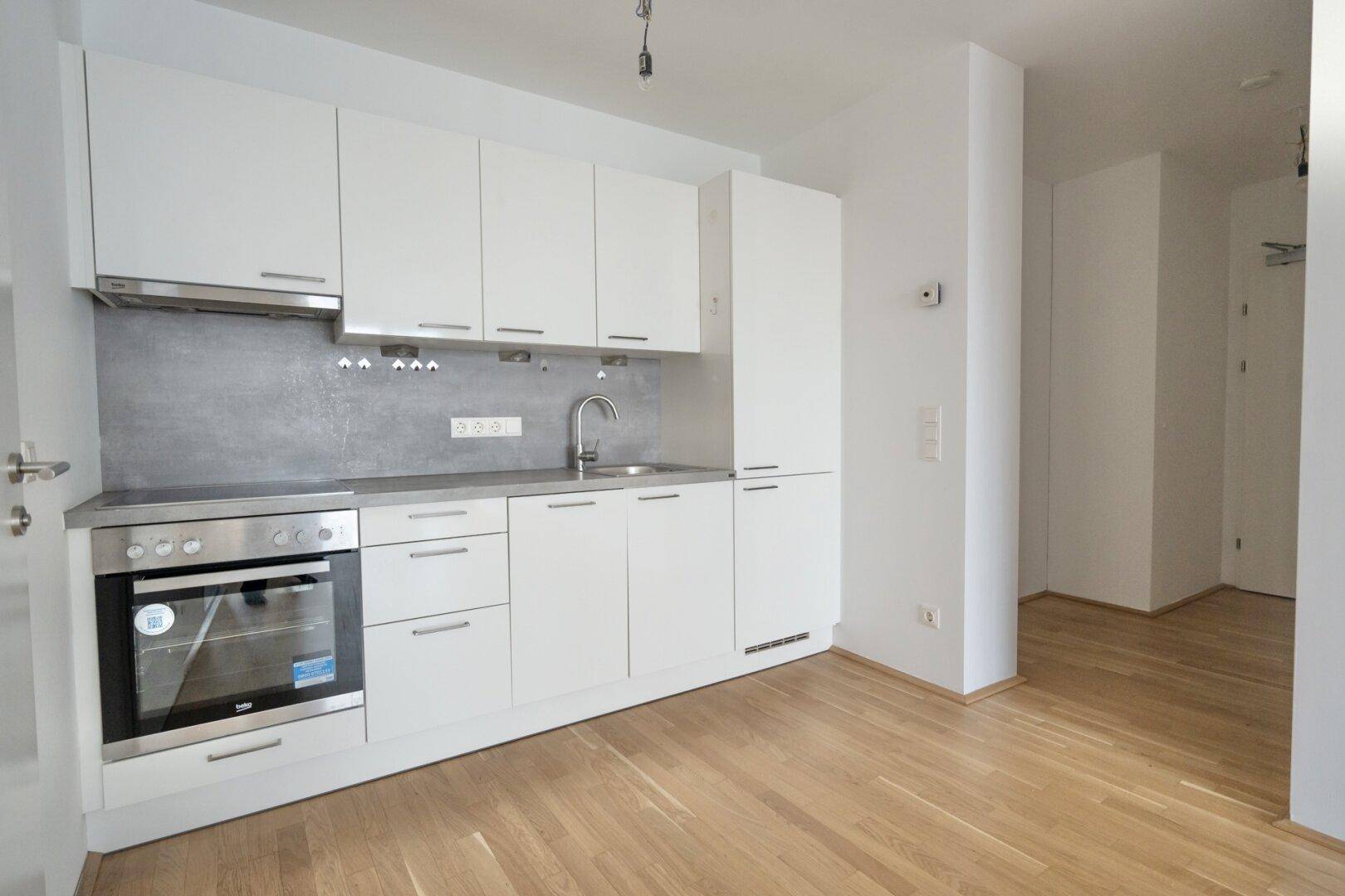 Moderne Einbauküche mit weißen Schränken, Edelstahlofen und hellem Holzboden.