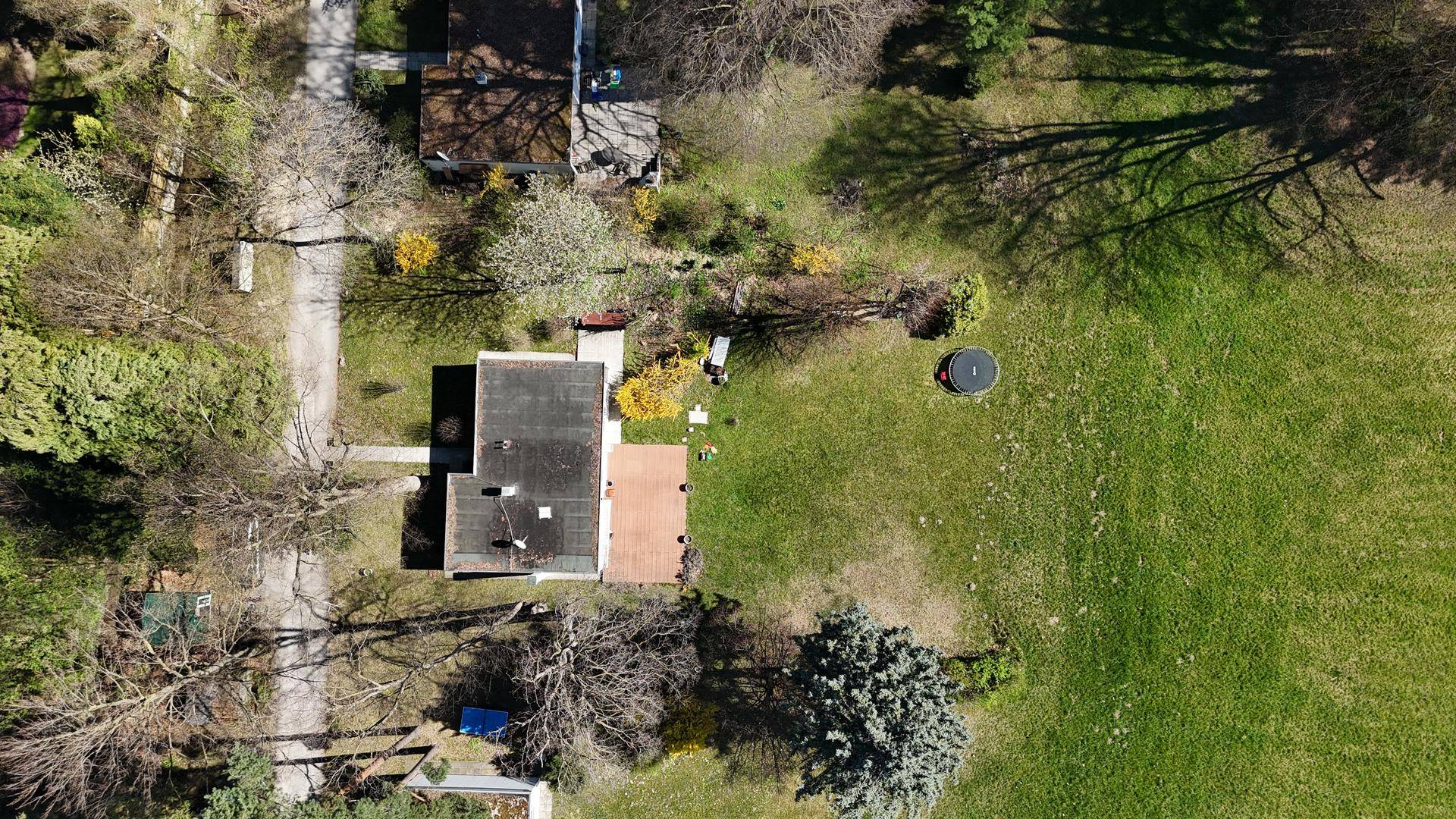 Vogelperspektive des Hauses mit Flachdach, Terrasse und dem weitläufigen Gartenbereich inklusive Trampolin.