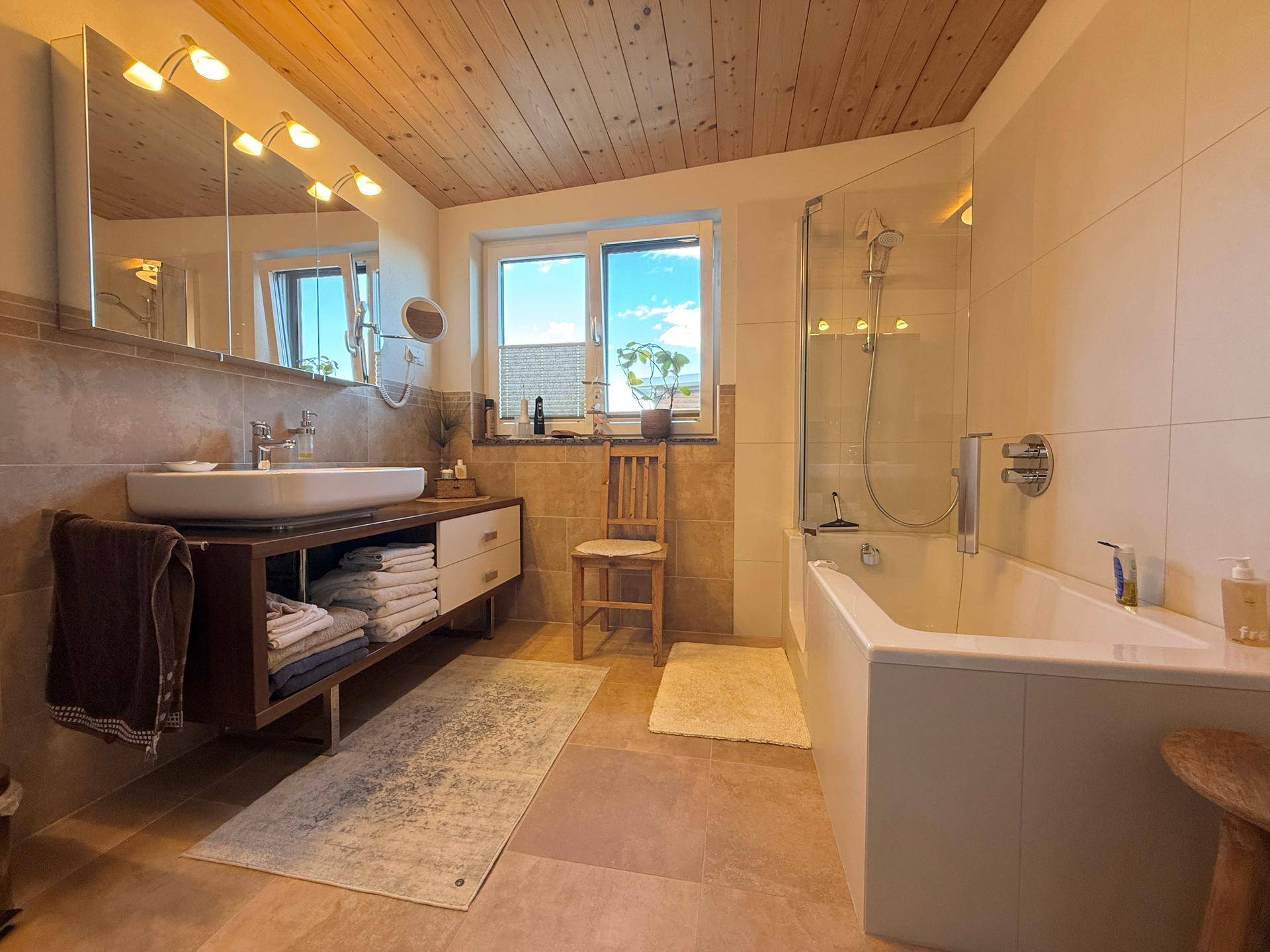 Modernes Badezimmer mit Badewanne, Dusche, Holzdecke und Fenster.