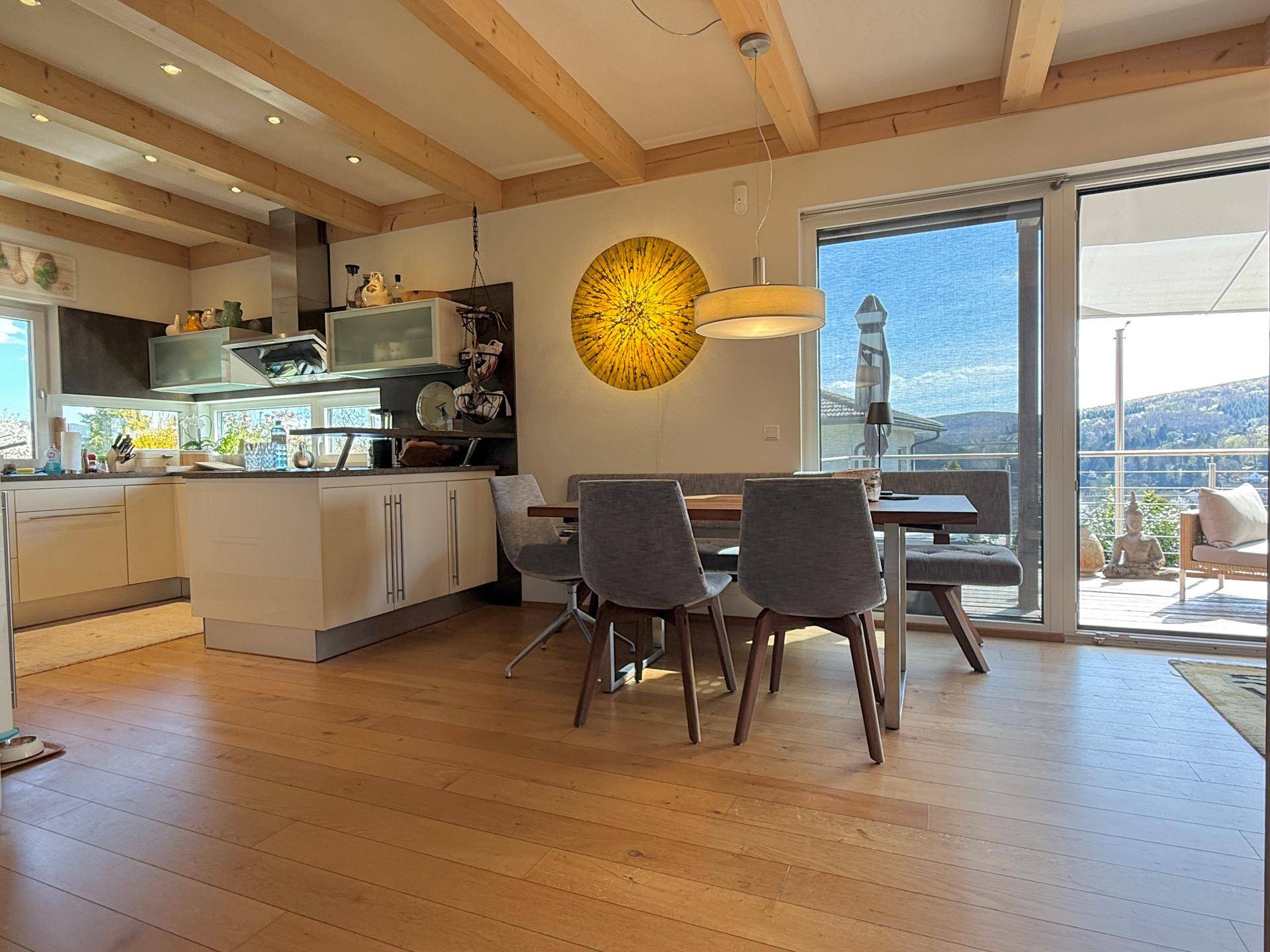 Offene Küche mit Essbereich, Holzbalken und Zugang zur Terrasse mit Weitblick.