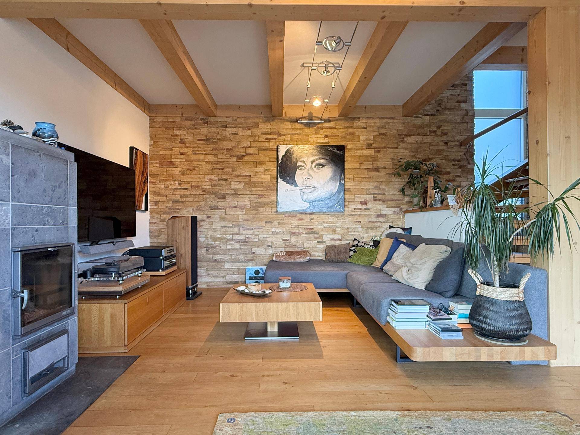 Gemütliches Wohnzimmer mit Holzboden, Kaminofen und dekorativer Steinwand.