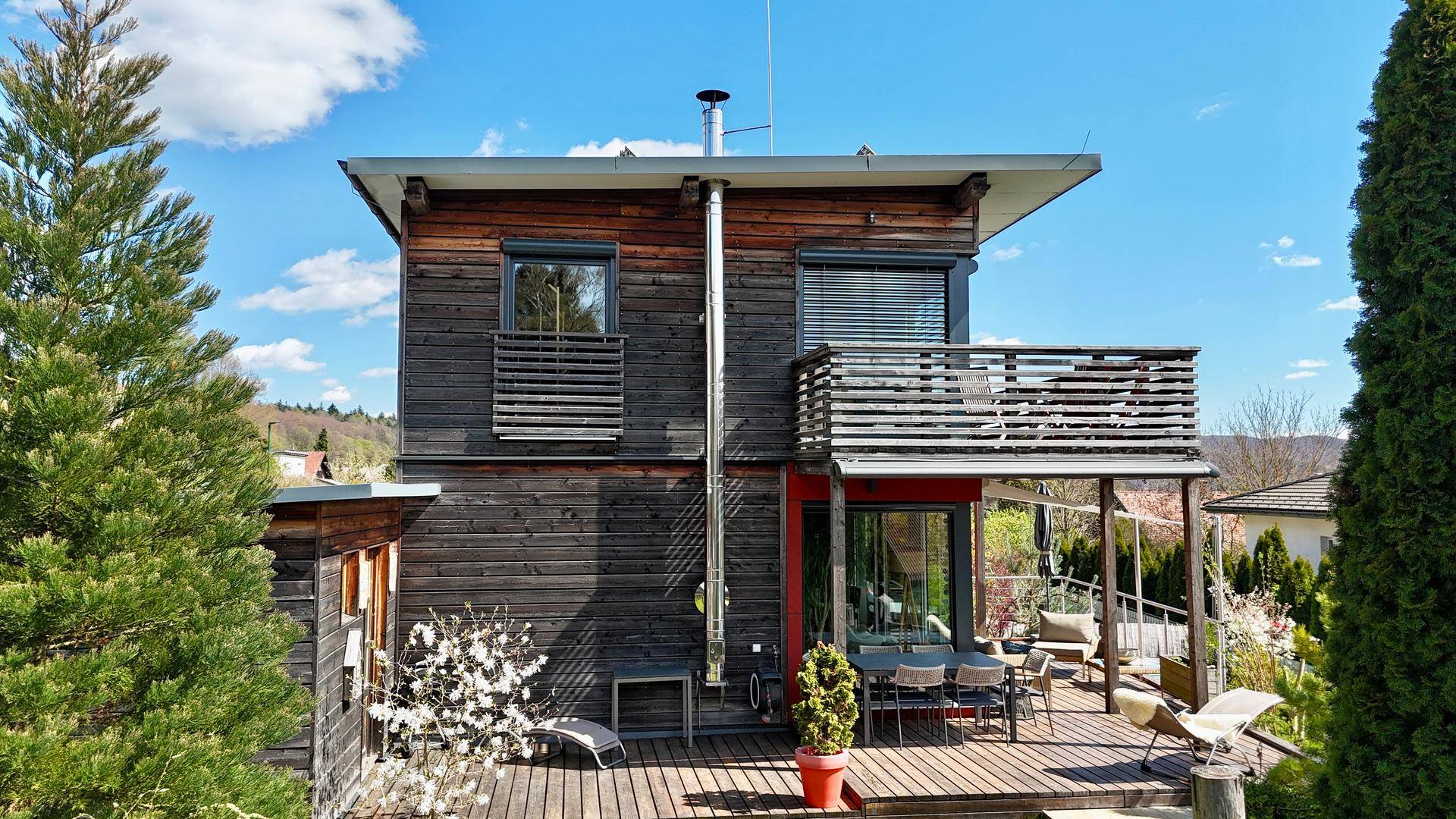 Rückansicht des modernen Hauses mit Holzfassade und großer Holzterrasse mit Sitzgelegenheiten.