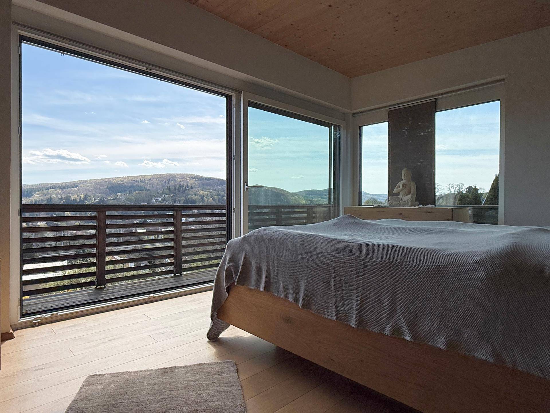 Helles Schlafzimmer mit Holzboden, großen Fenstern und Balkonzugang mit Bergblick.