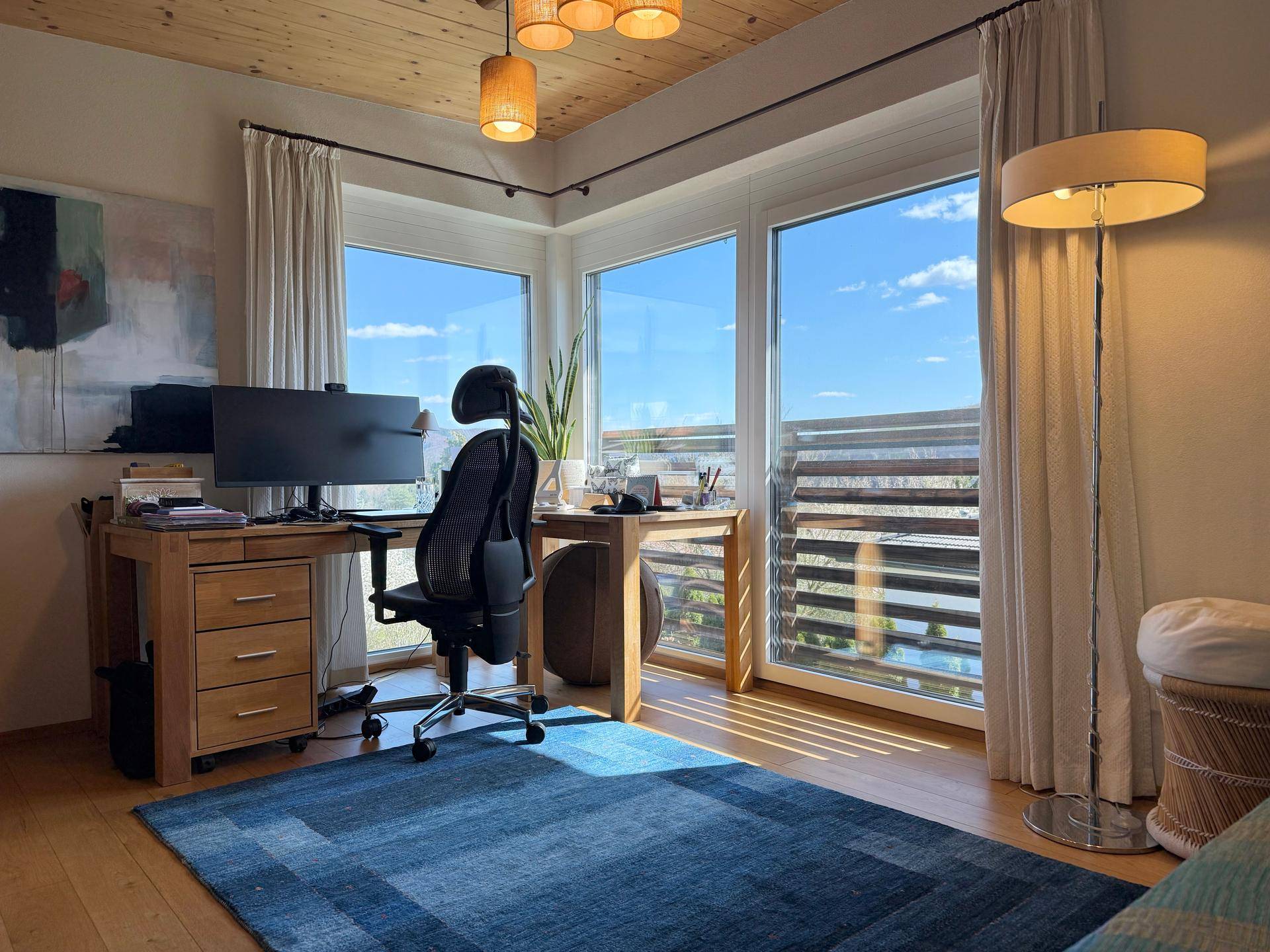 Helles Arbeitszimmer mit Holzboden, großen Fenstern und Blick ins Grüne.