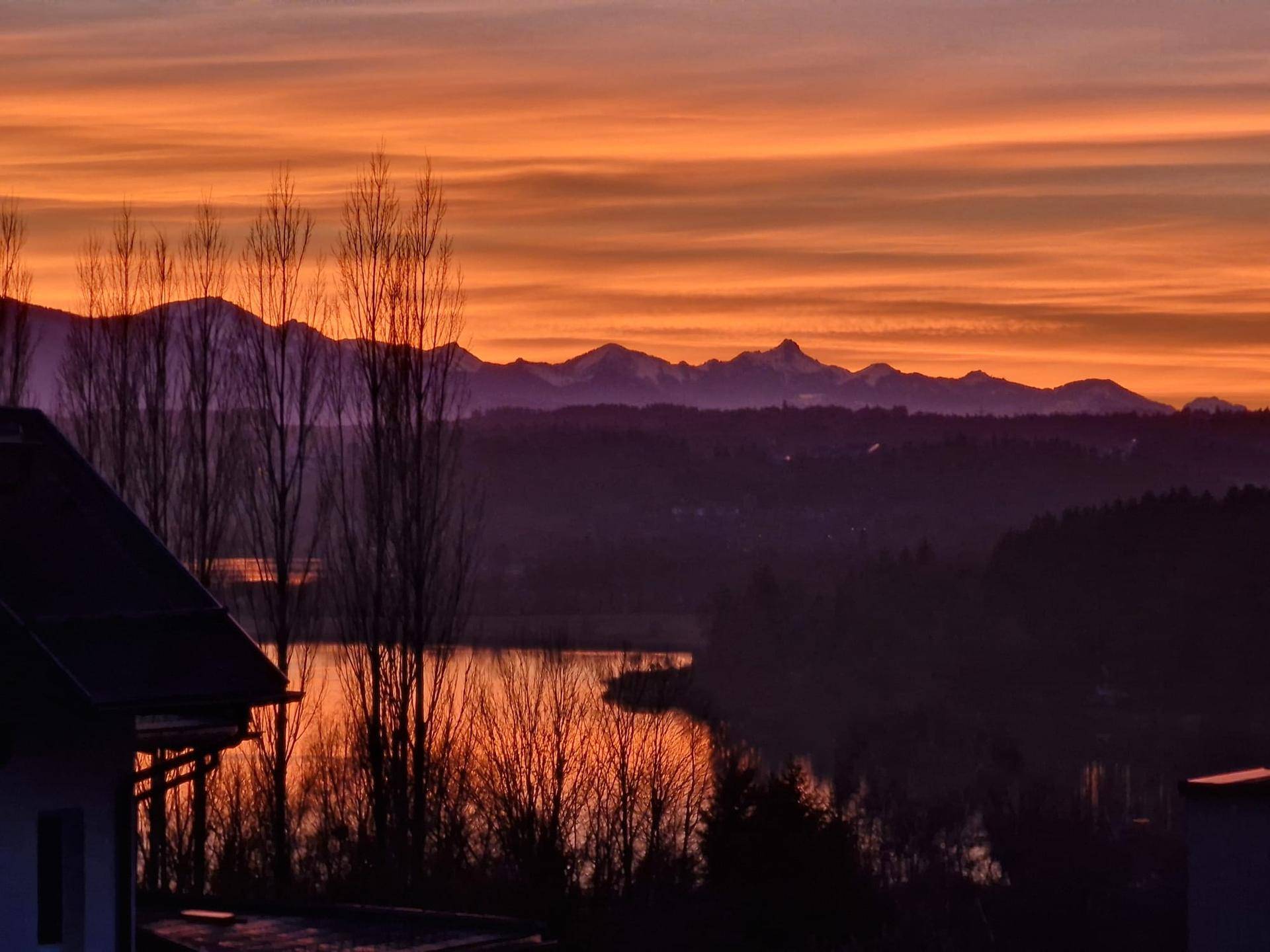 Malerischer Sonnenuntergang über Bergen und See, mit dramatischer Himmelsfärbung.