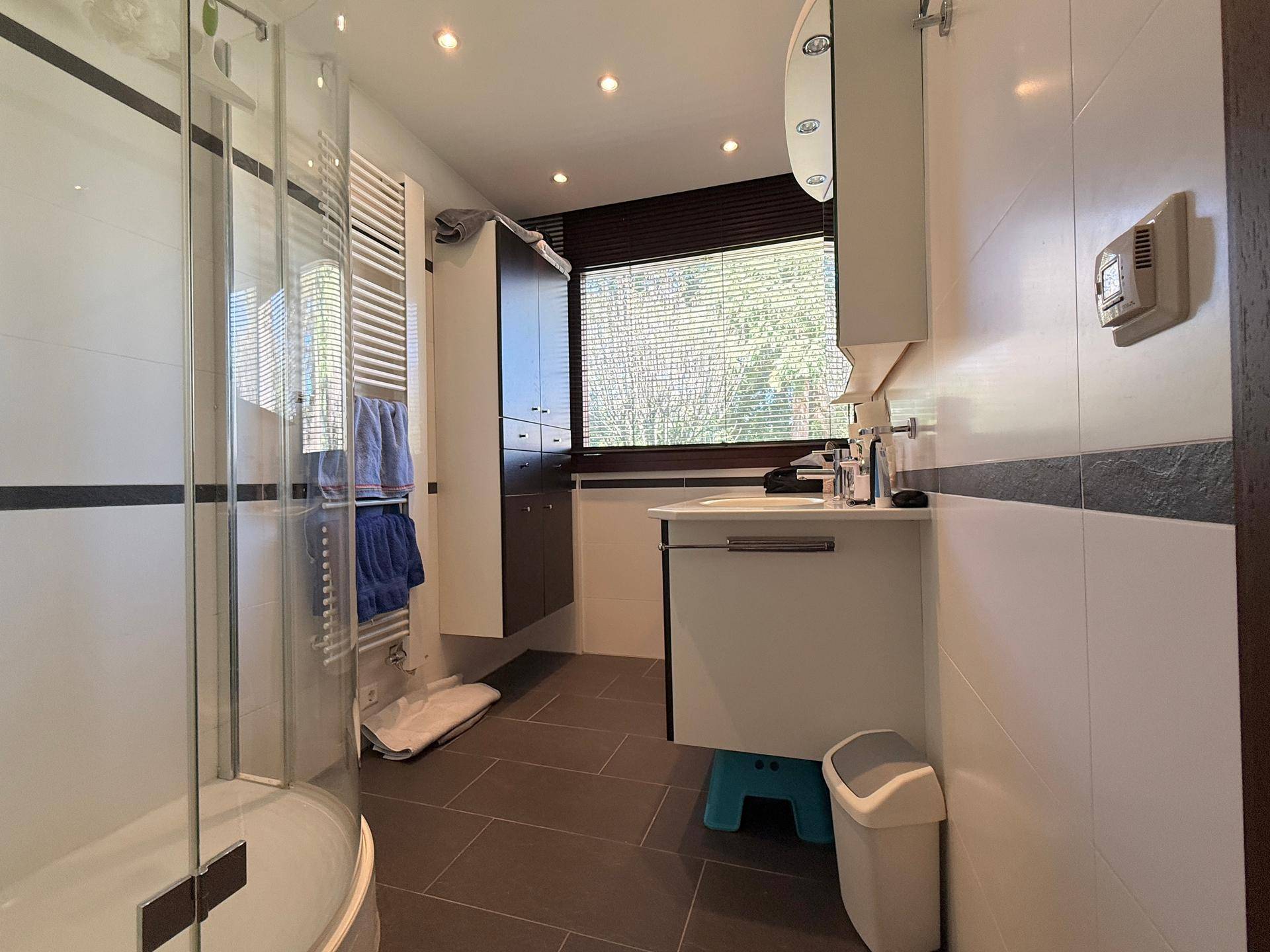 Modernes Badezimmer mit Duschkabine, Einzelwaschbecken, beheiztem Handtuchhalter und Fenster.