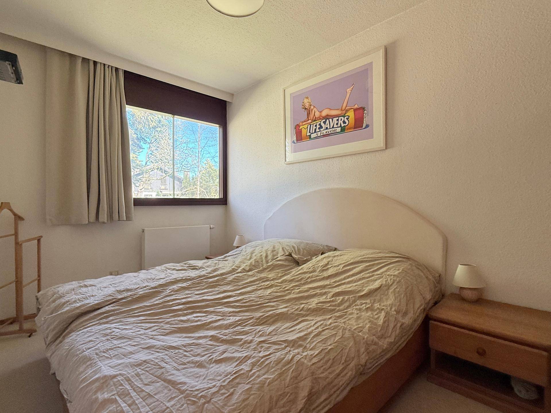 Schlafzimmer mit Doppelbett, Teppichboden und einem Fenster, das den Raum hell erscheinen lässt.