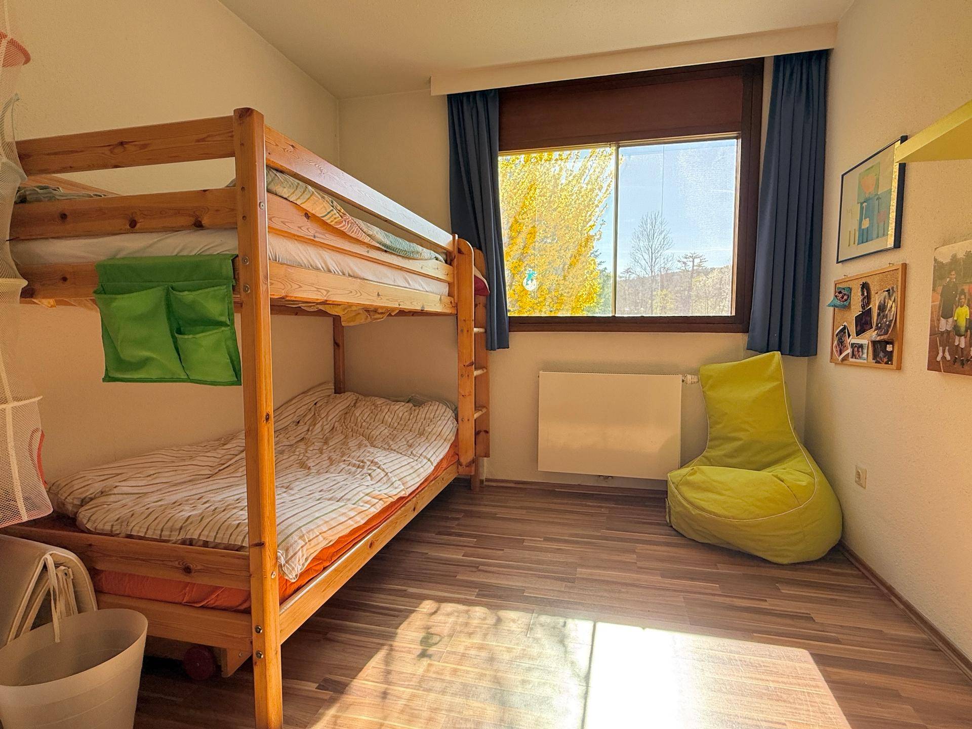 Kinderzimmer mit Etagenbett, Laminatboden und einem Fenster, das viel Tageslicht hereinlässt.