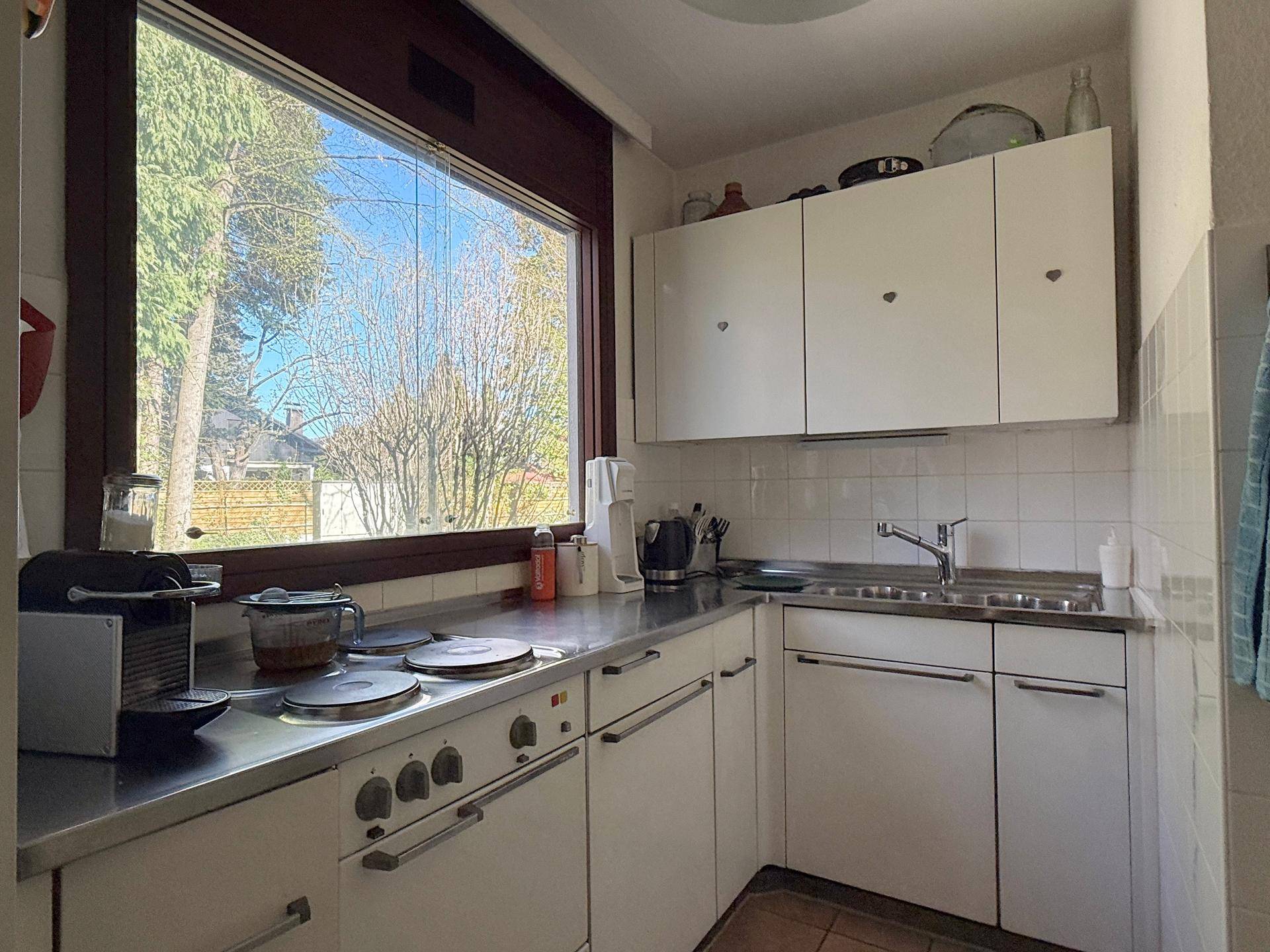 Funktionale Küche mit weißen Schränken, Edelstahl-Arbeitsplatte und großem Fenster mit Ausblick.