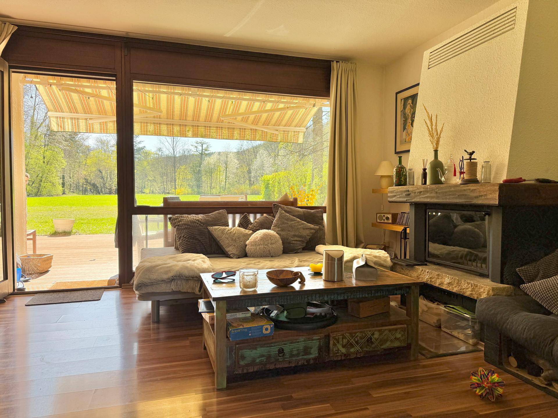Helles Wohnzimmer mit Kamin, Holzboden und großem Fenster mit Zugang zur Terrasse.