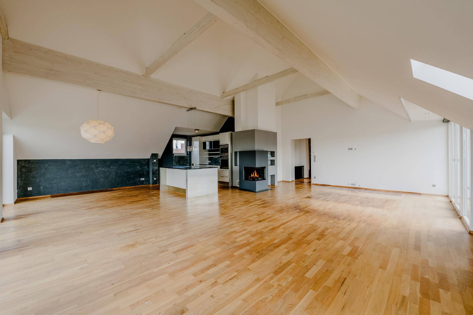 Großzügiges Dachgeschoss mit Holzboden, Kamin und offener Küche in heller Atmosphäre.