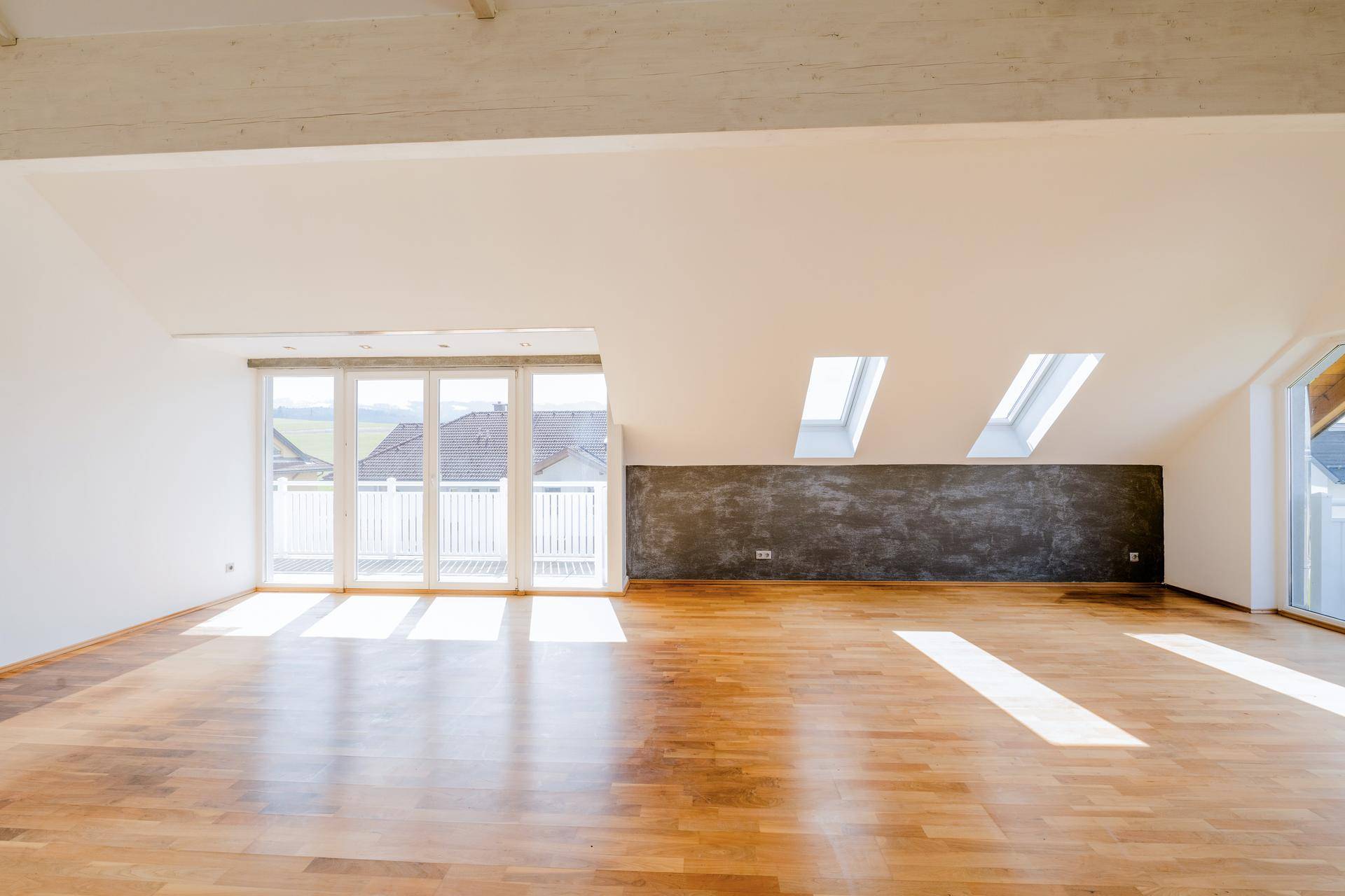 Heller Raum mit Holzboden, Dachfenstern und Zugang zu einem Balkon.