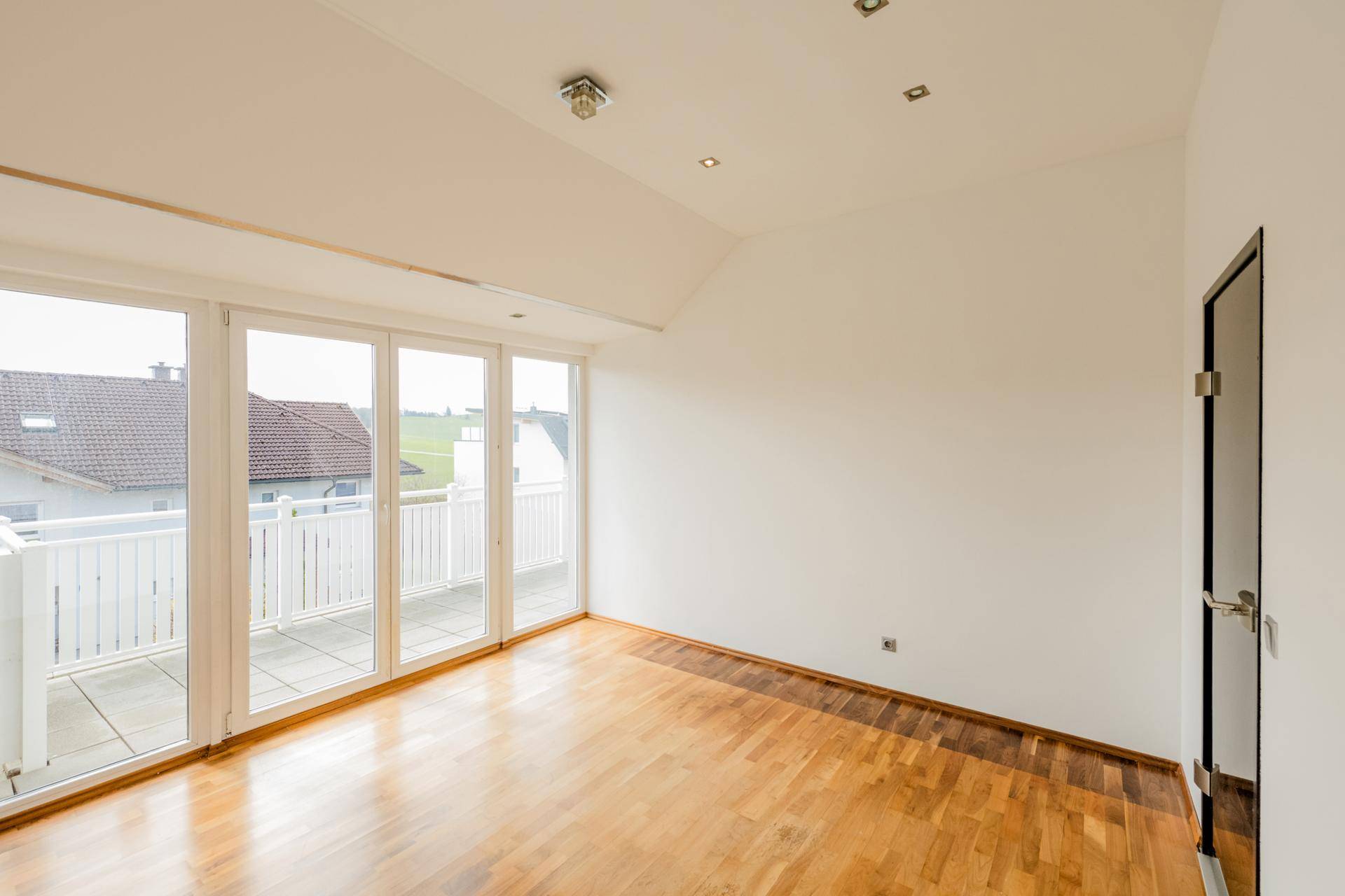 Geräumiger Raum mit Holzboden, Einbaustrahlern und Zugang zu einem Balkon.