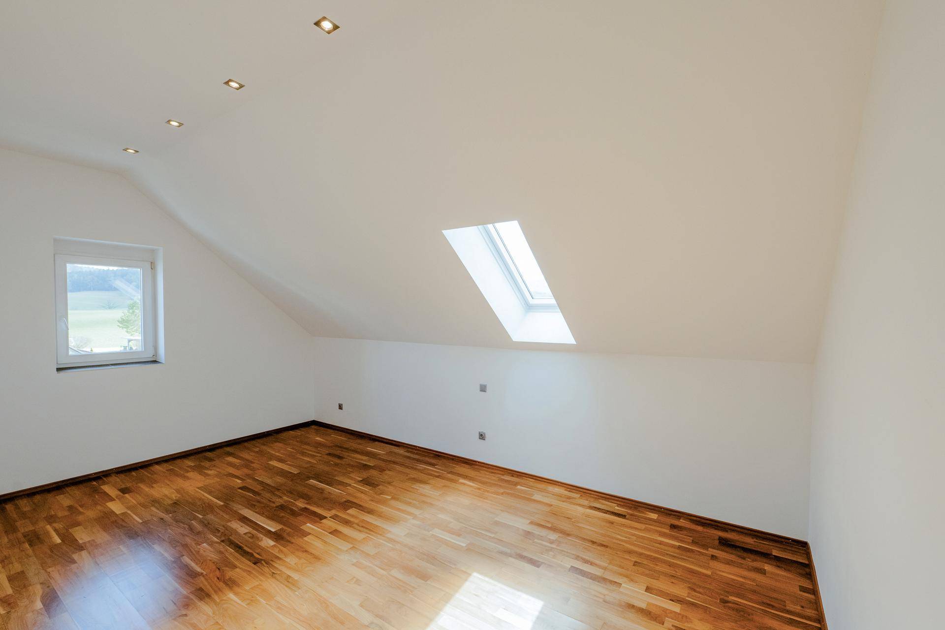 Heller Raum mit Holzboden, Fenster und Dachfenster für viel Tageslicht.